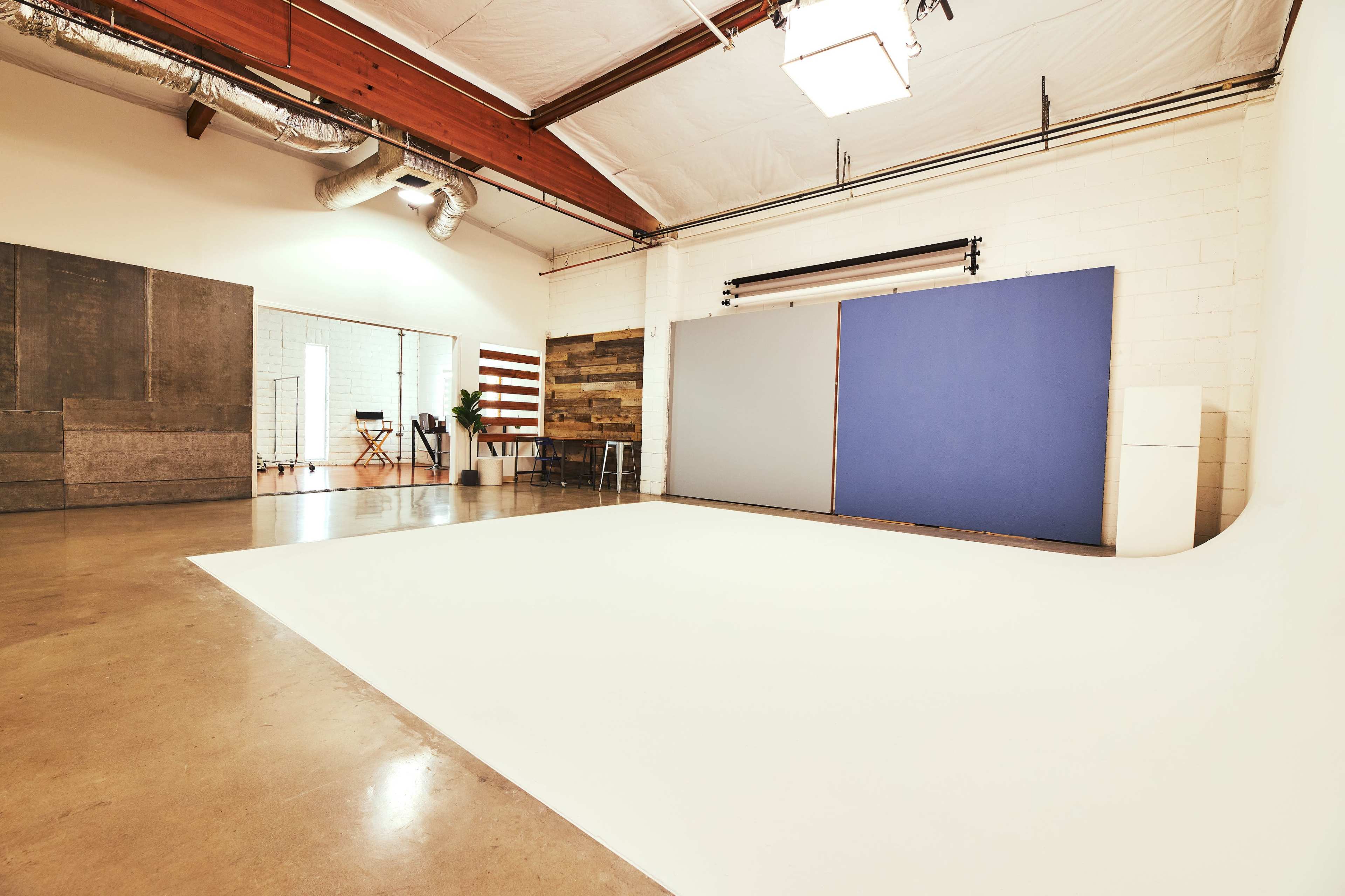 A spacious photography studio with a white backdrop, concrete walls, and various colored panels.
