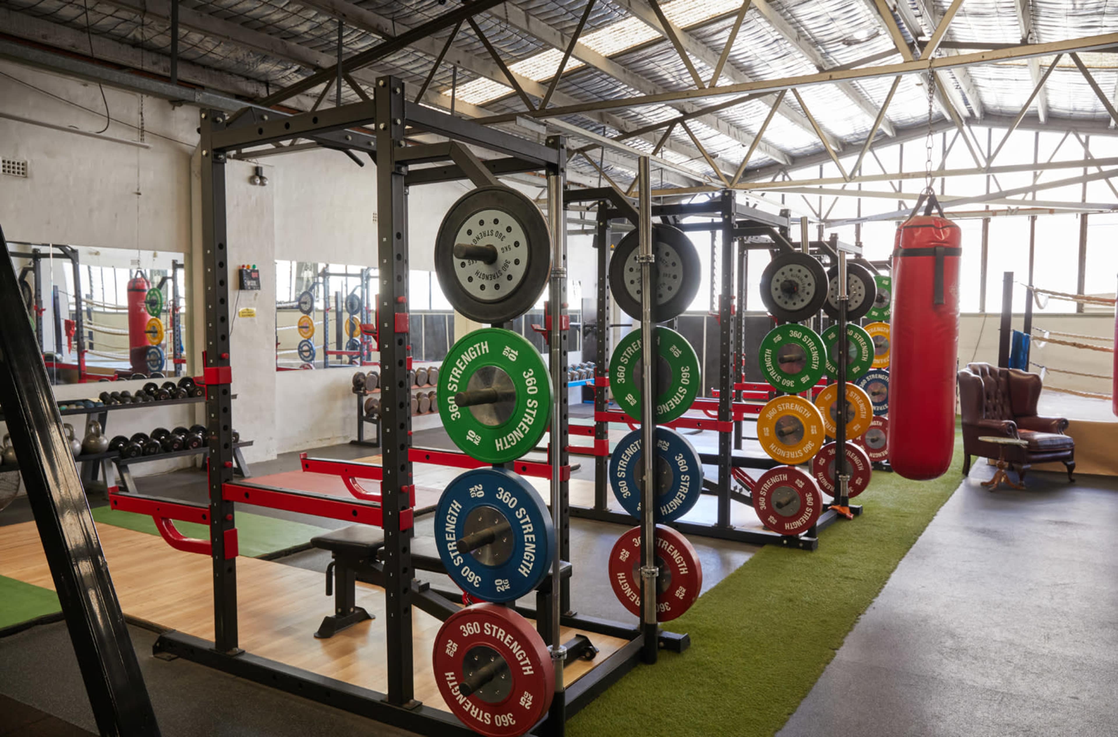 A gym interior with weightlifting equipment, including barbells with color-coded plates and a red punching bag in the background.