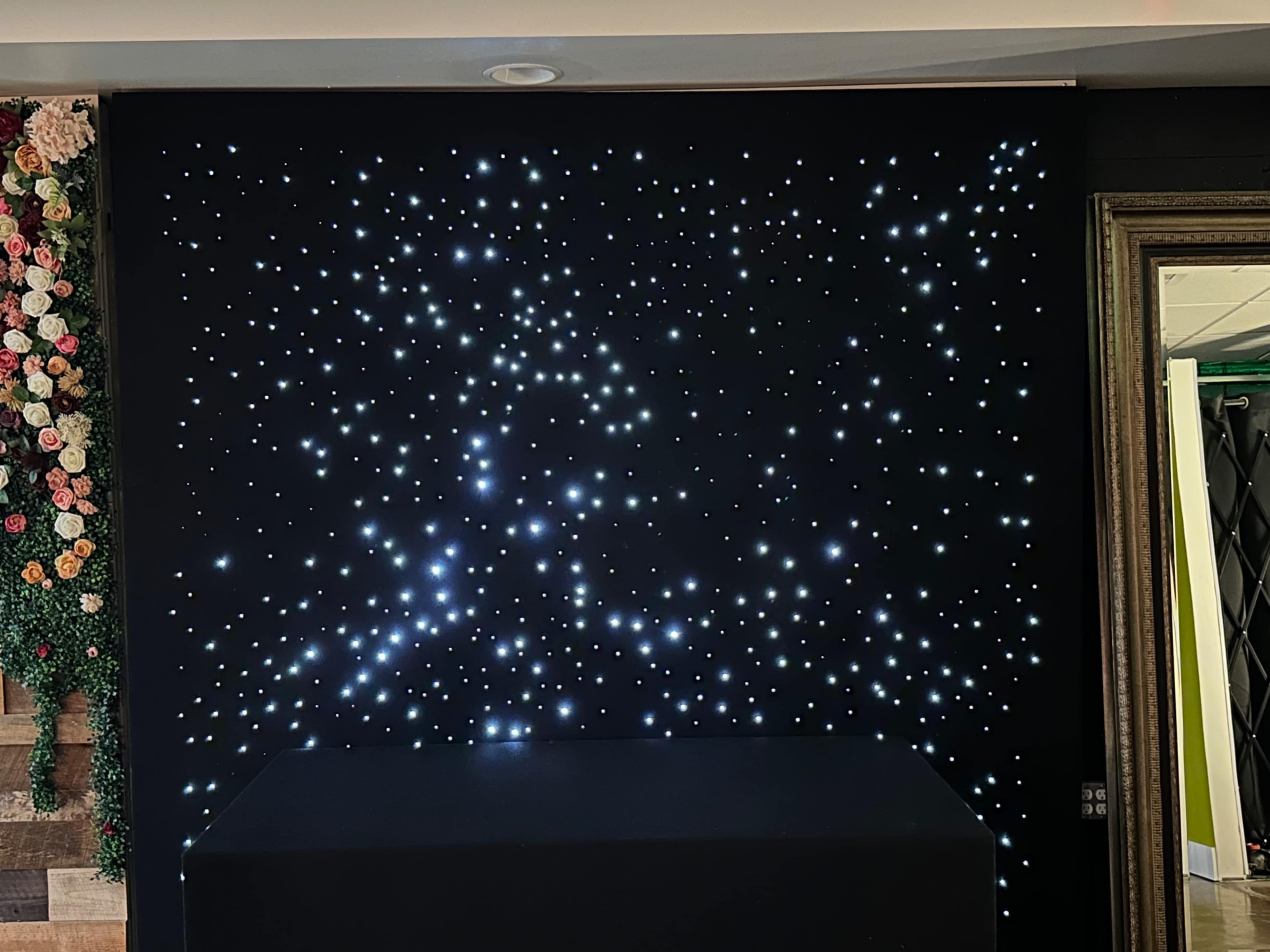 The image features a black wall adorned with numerous small white lights that resemble stars, accompanied by a dark table in the foreground.