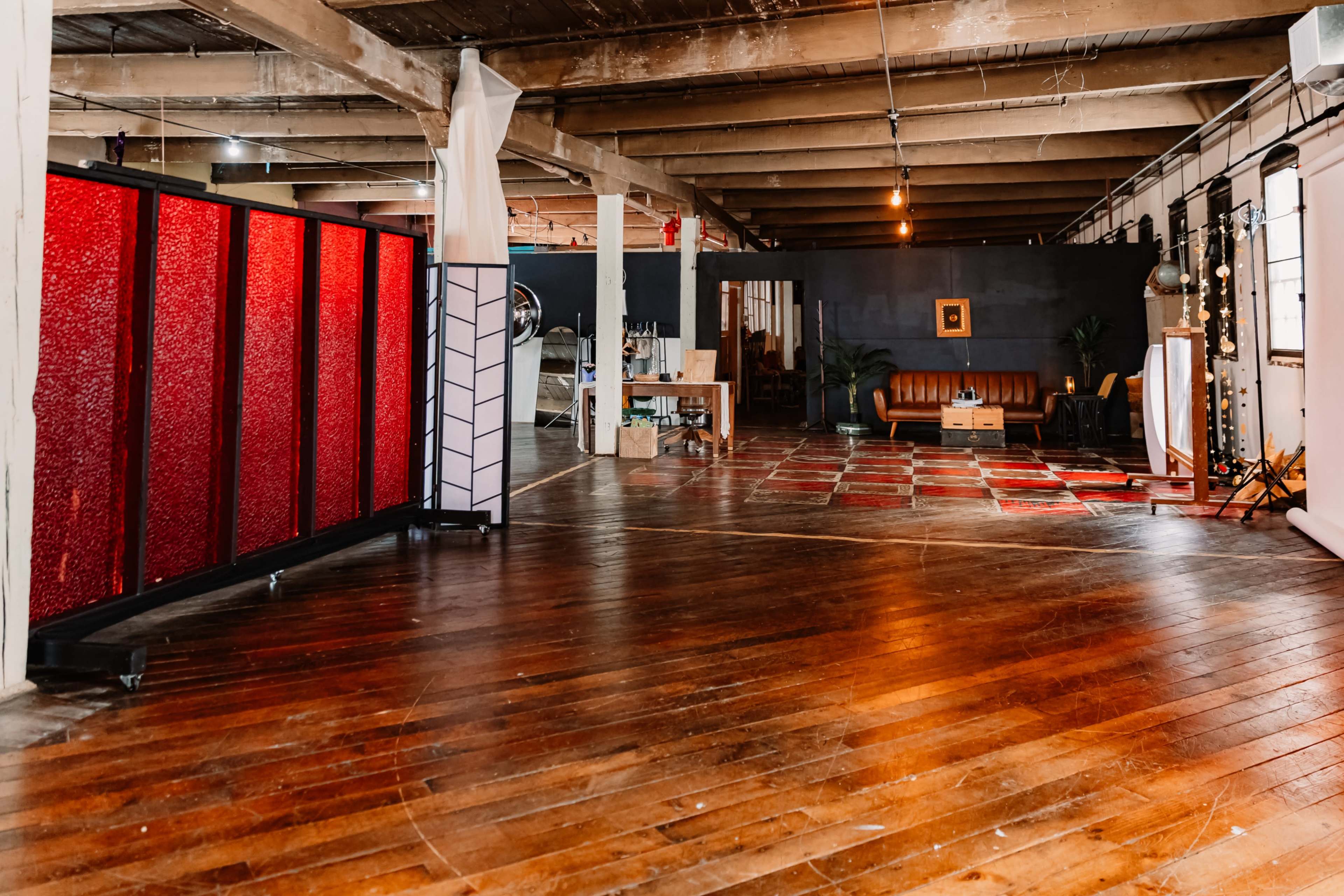 The image shows an expansive indoor space featuring wooden flooring, red and black partition screens, a brown sofa, and various lighting setups.