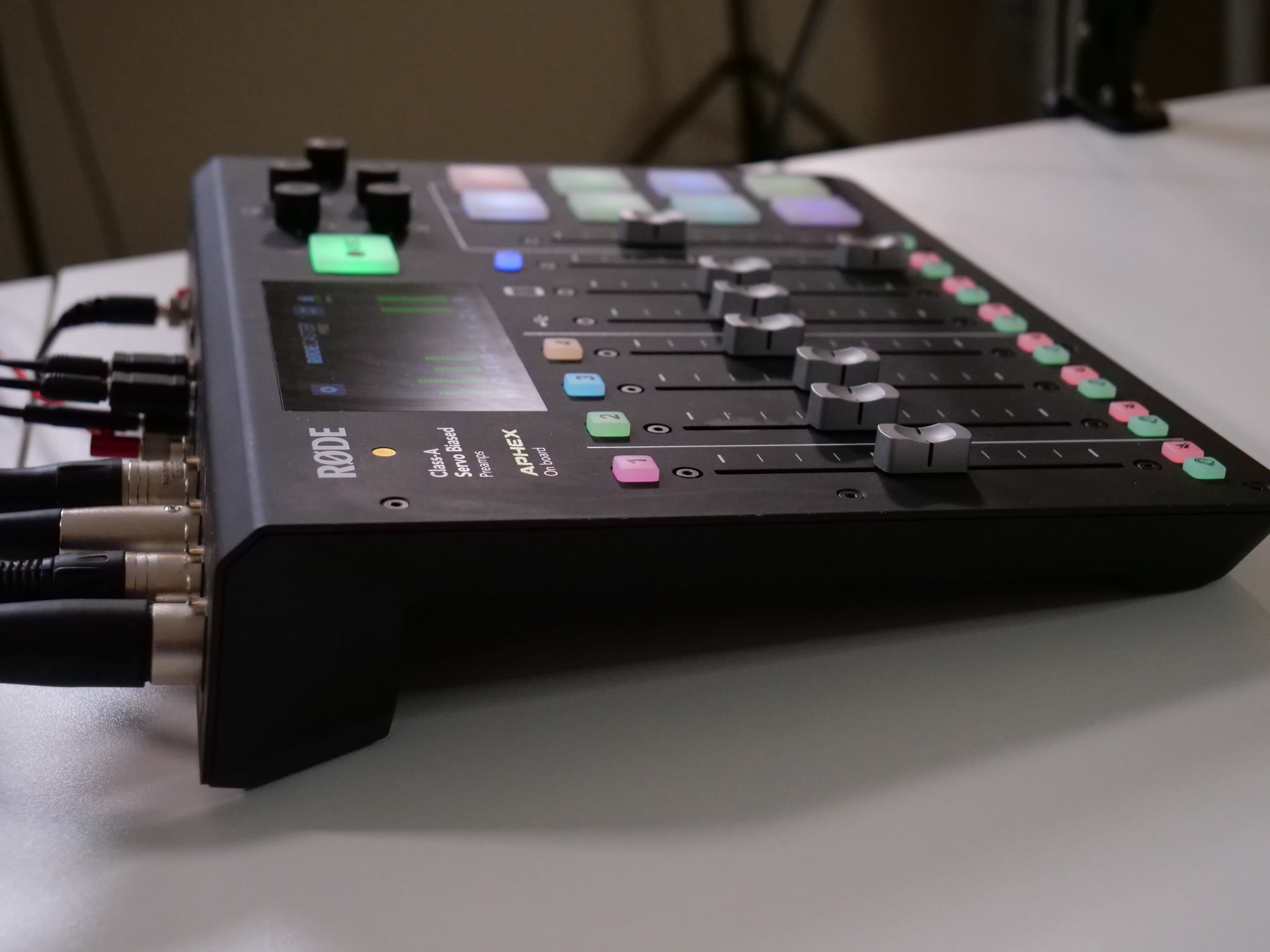 A Rode audio mixer with multiple sliders and buttons is positioned on a table, surrounded by audio cables.
