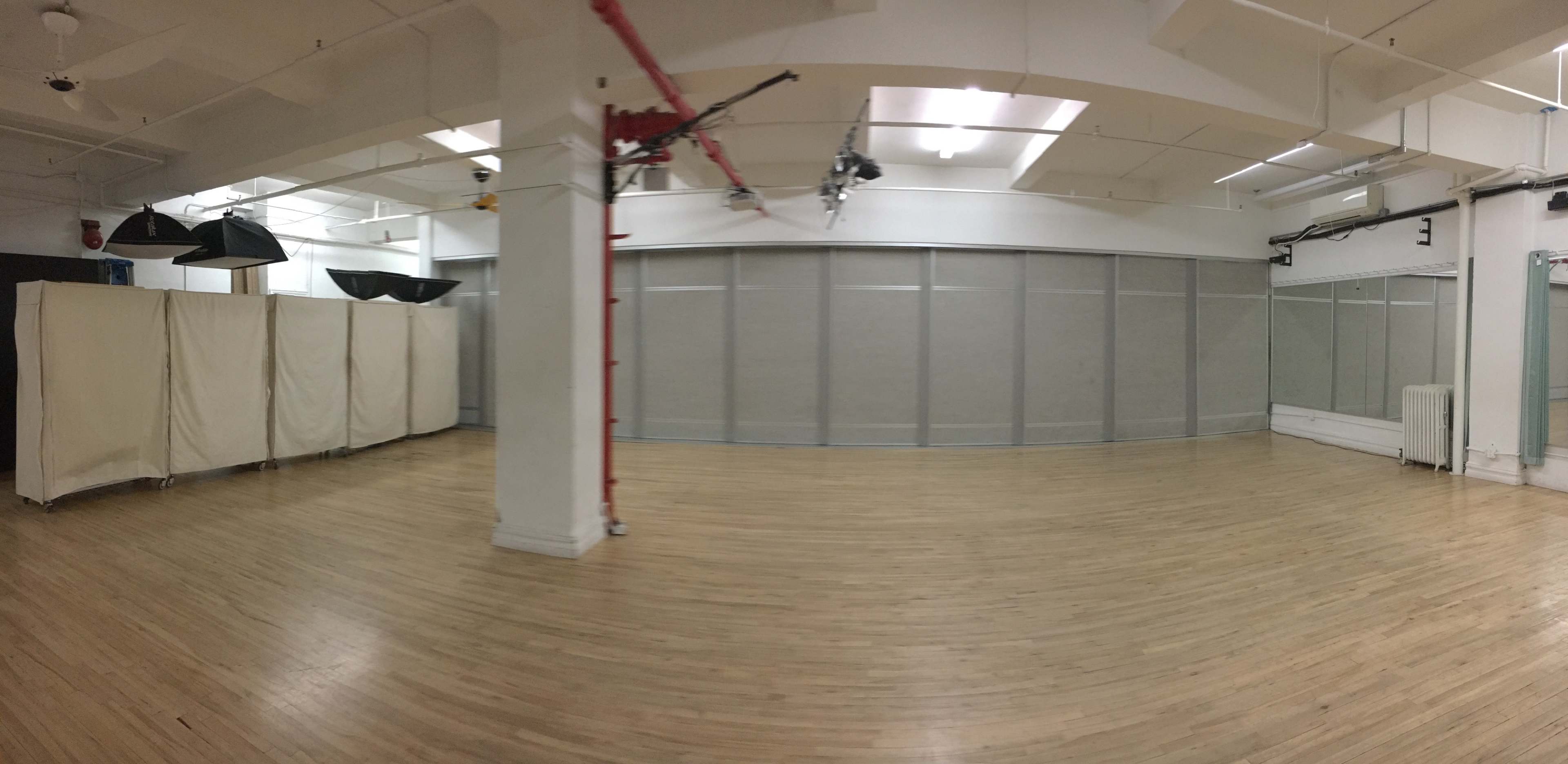 The image shows a spacious, empty studio with wooden flooring and large gray partitions.