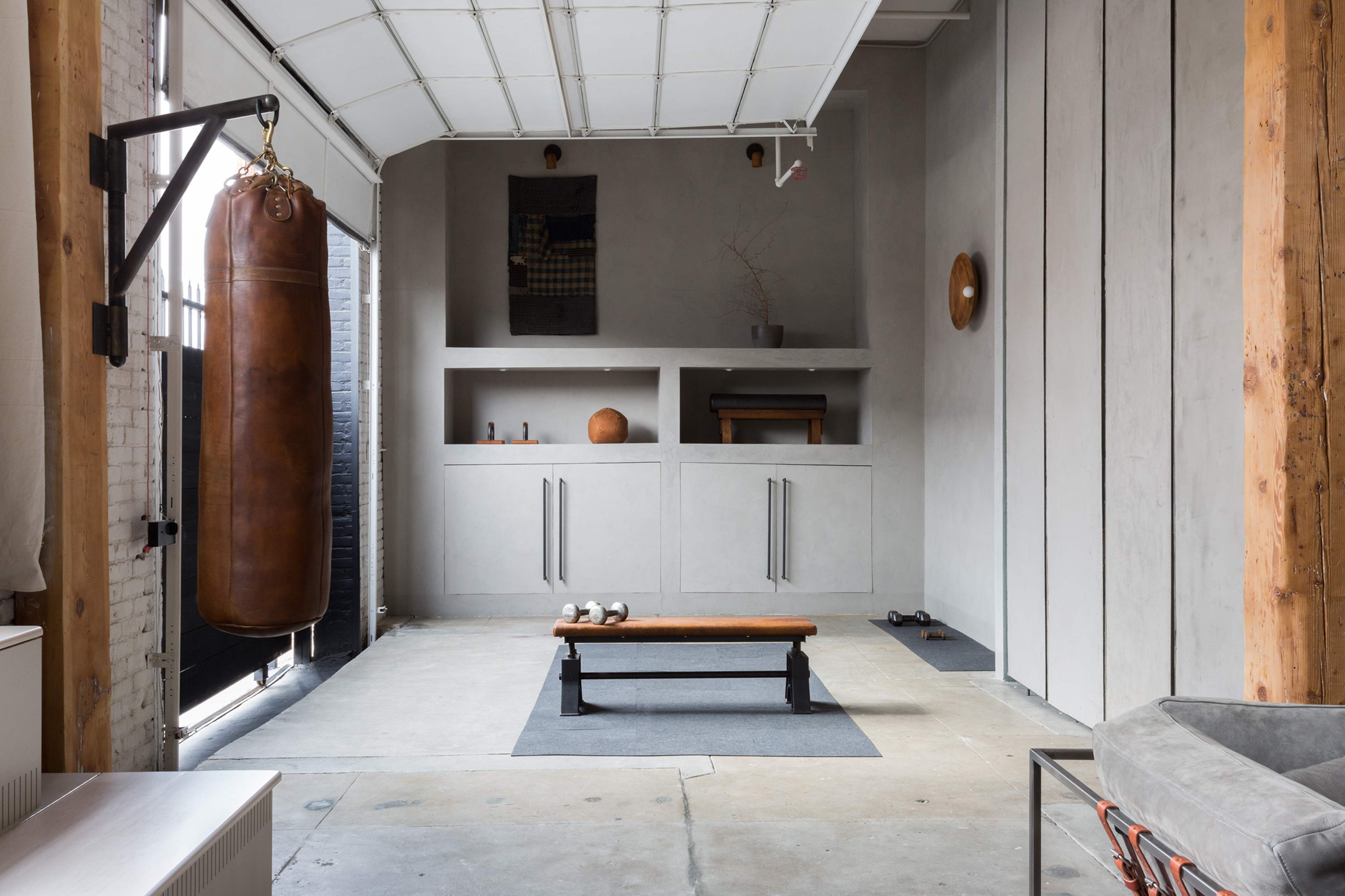 The image shows a minimalist home gym with a punching bag, a weight bench, and a concrete wall shelf.
