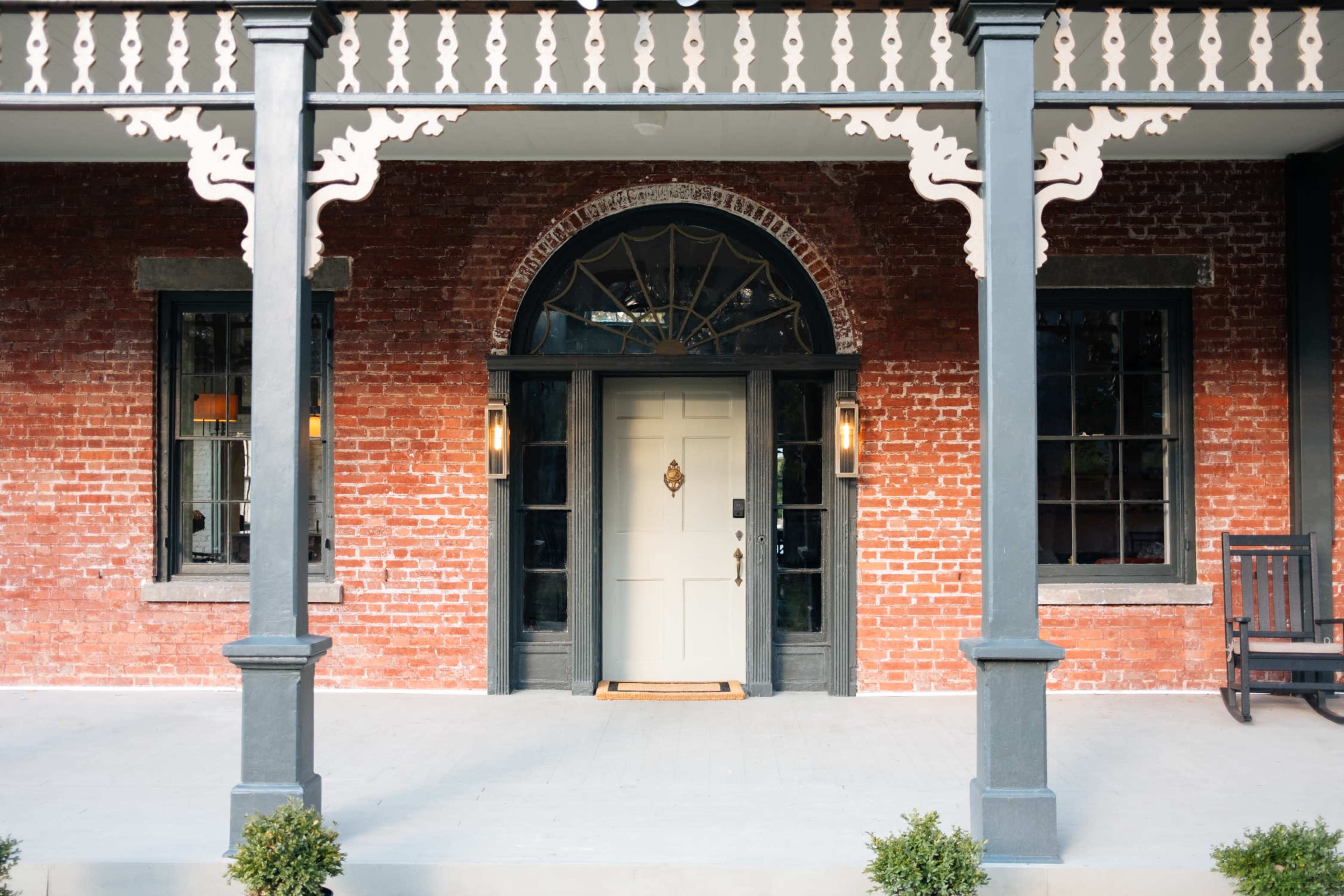 A brick building with a white front door framed by large windows and decorative columns.