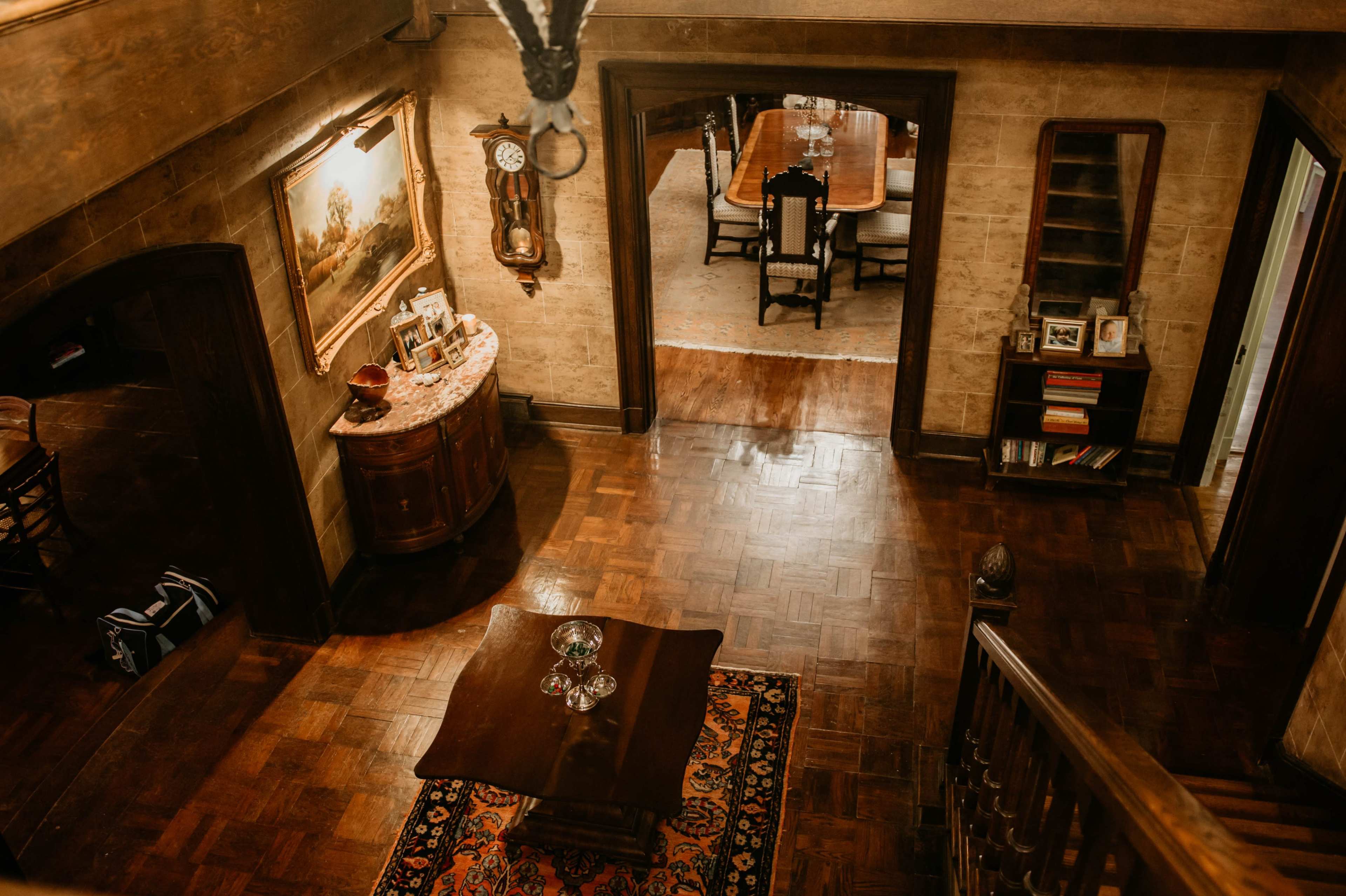 An overhead view of a room featuring wooden flooring, a table with decorative items, a large painting, and a dining area in the background.