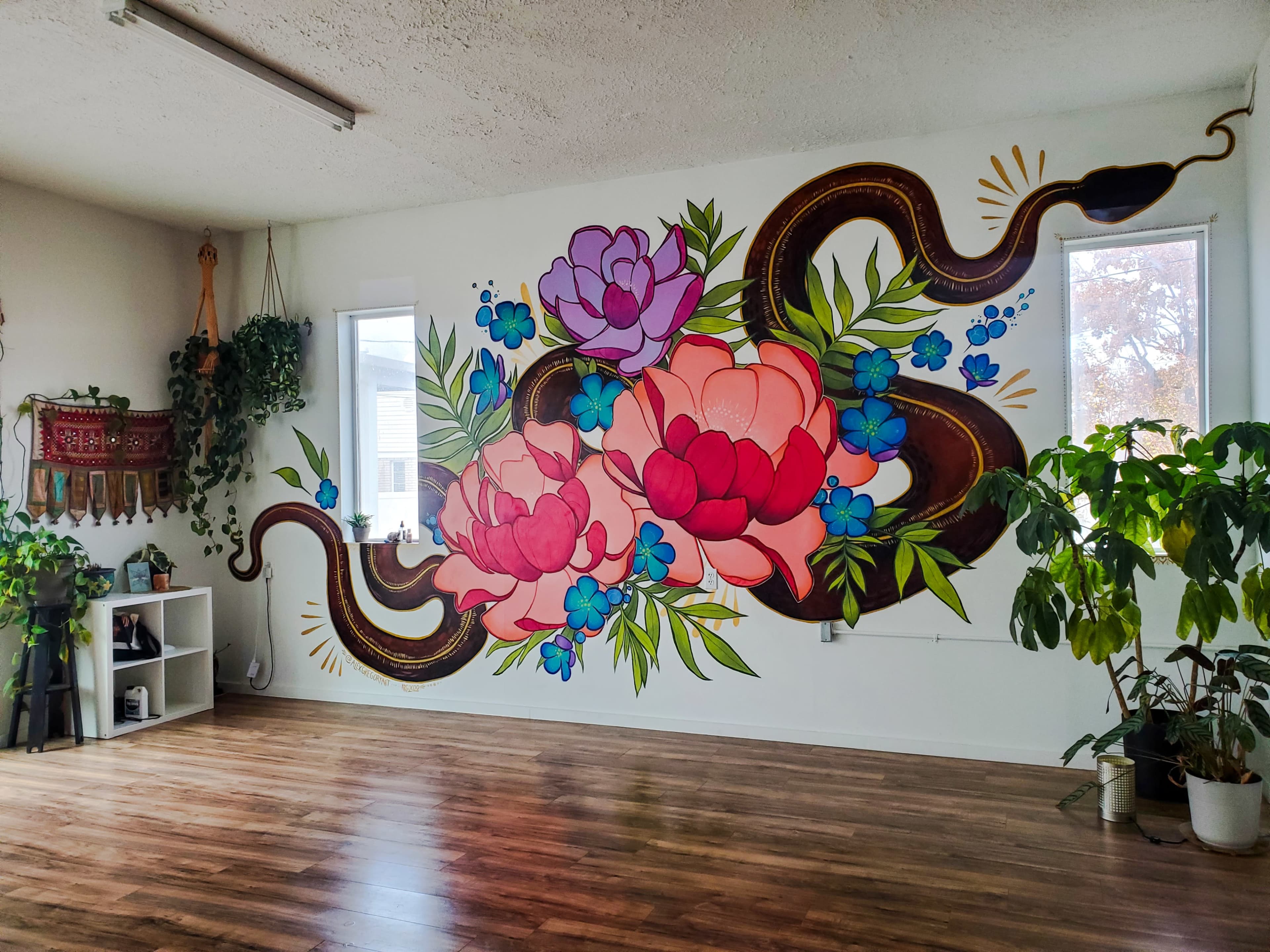 A large, vibrant mural of flowers and a snake on a wall in a room with natural light and wooden flooring.