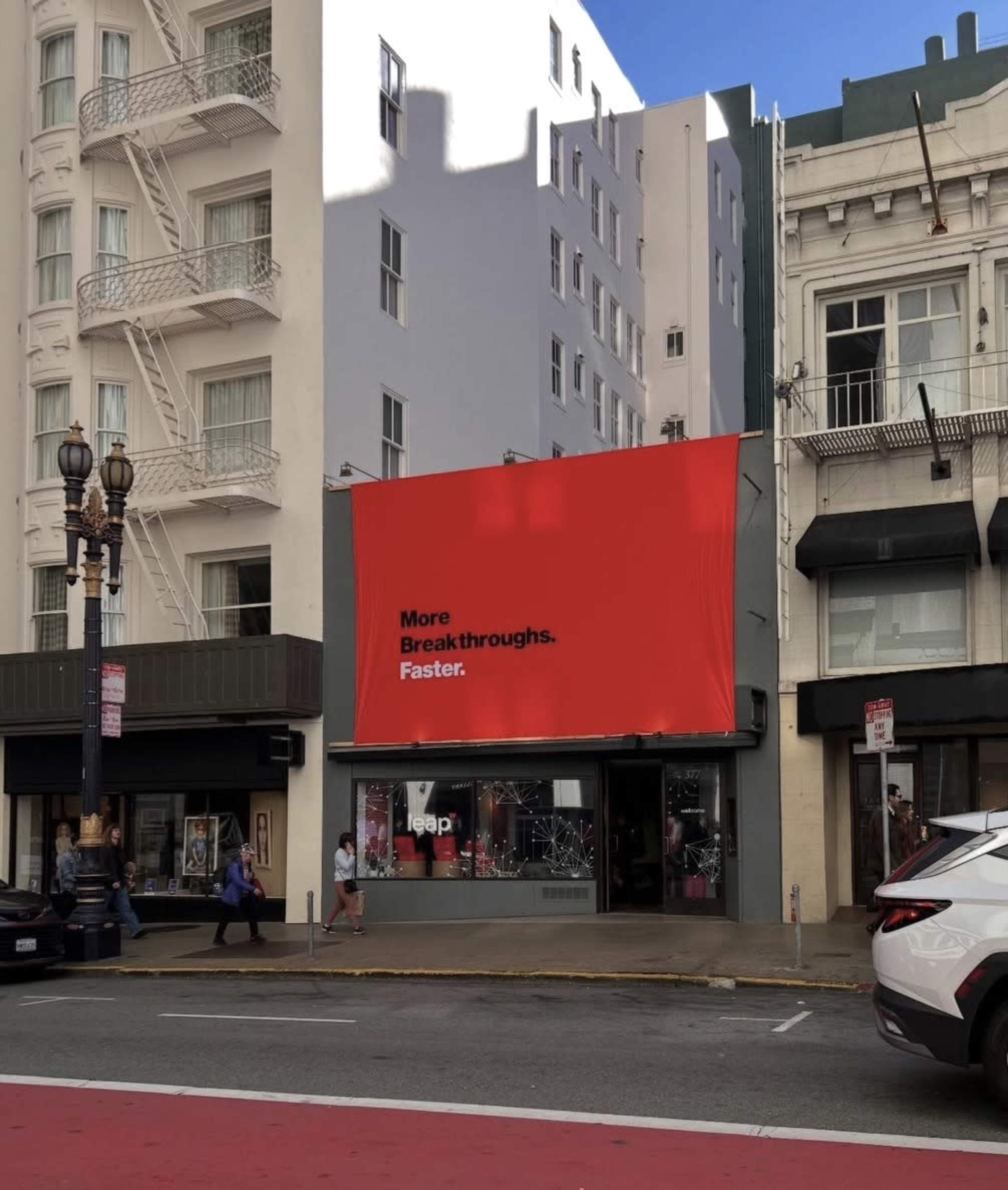 A large red billboard with the text "More Breakthroughs. Faster." is displayed on the side of a building in an urban setting.