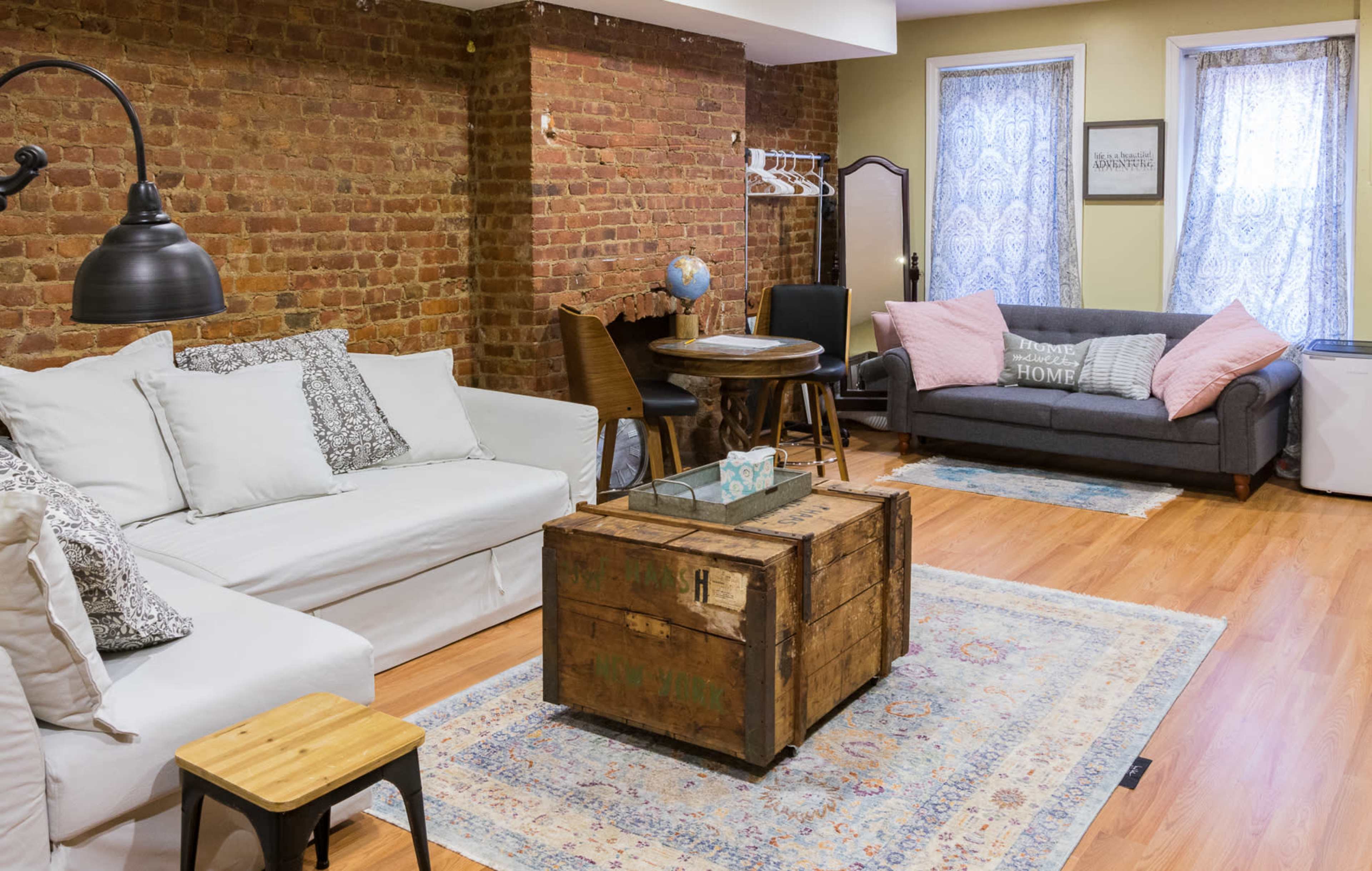A cozy living room featuring a white sofa, a gray couch, a wooden coffee table, and exposed brick walls.