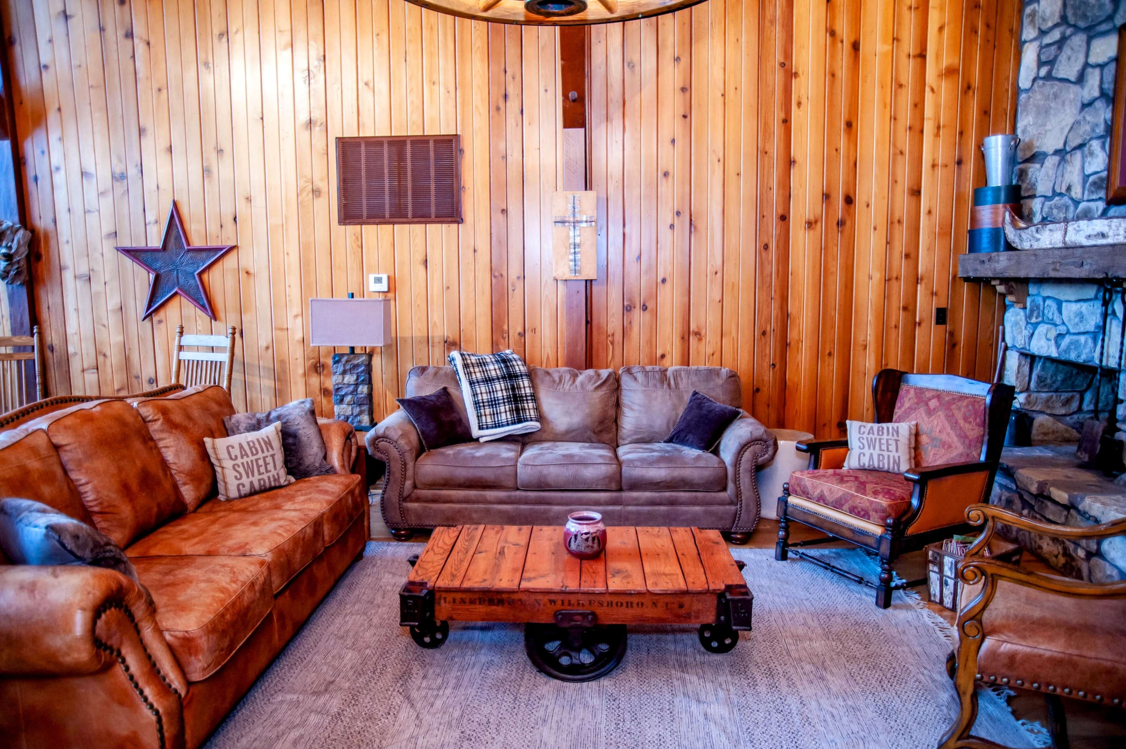 A cozy living room featuring leather sofas, a wooden coffee table on castor wheels, and a stone fireplace against a backdrop of wooden walls.