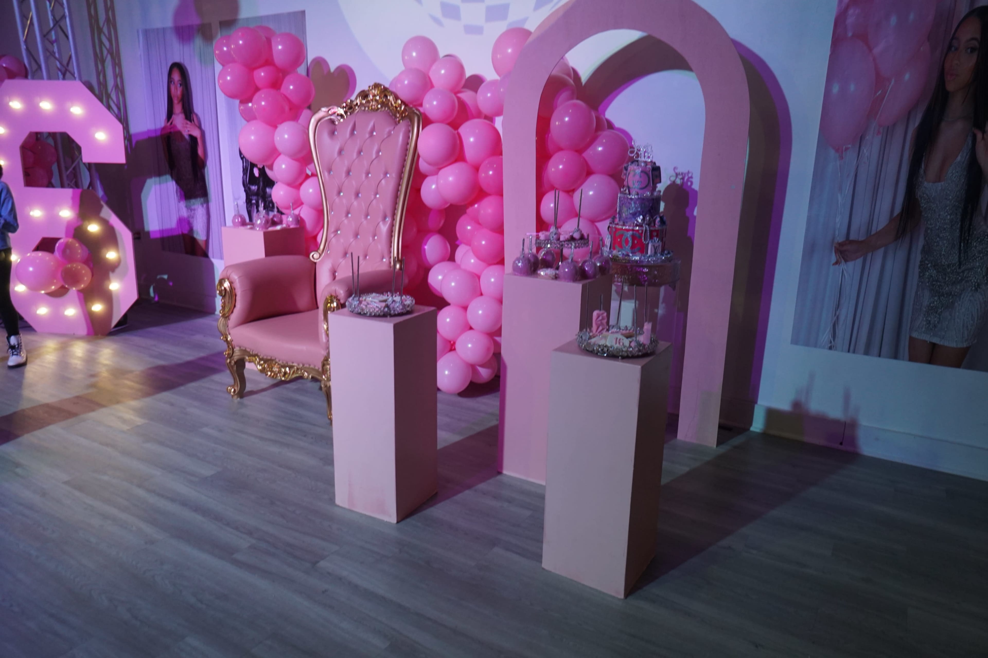 The scene features a pink-themed setting with a large ornate chair, two pink pedestals displaying treats, and a backdrop of pink balloons.