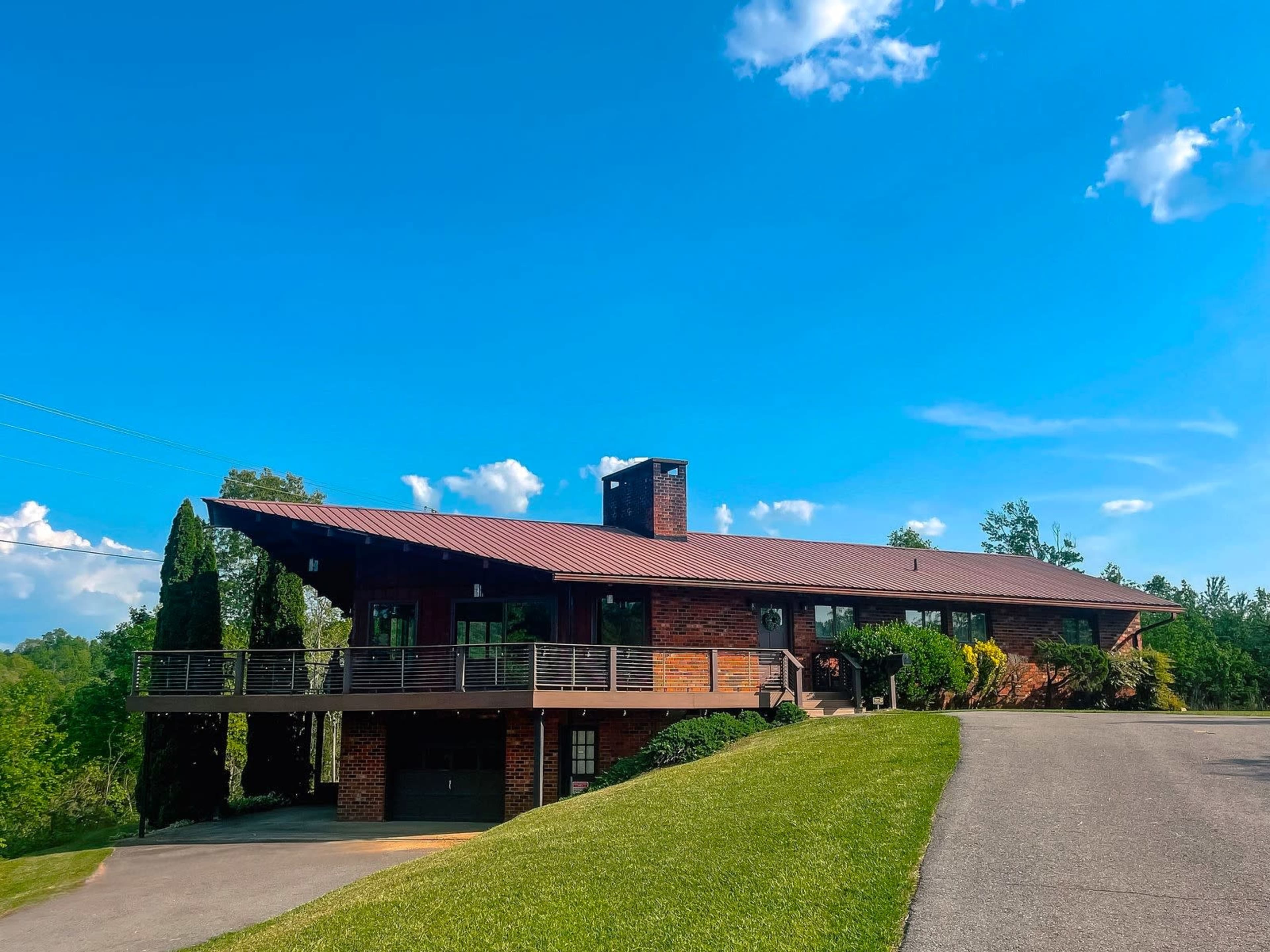 A large brick house with a sloped roof is situated on a grassy hillside under a blue sky.
