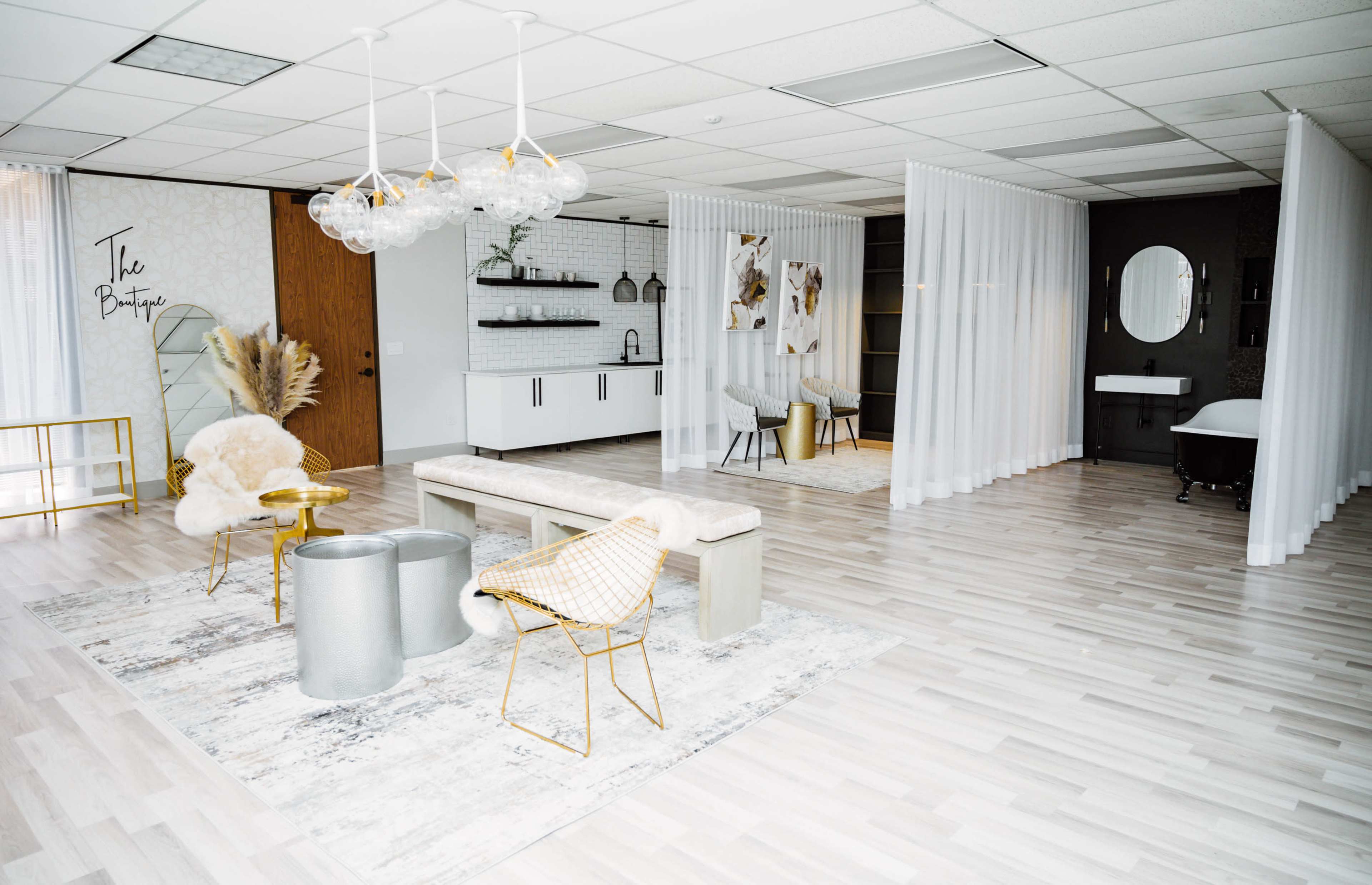 A modern, stylish interior space with light wooden flooring, a seating area featuring a bench and decorative chairs, and partitioned sections for different uses.