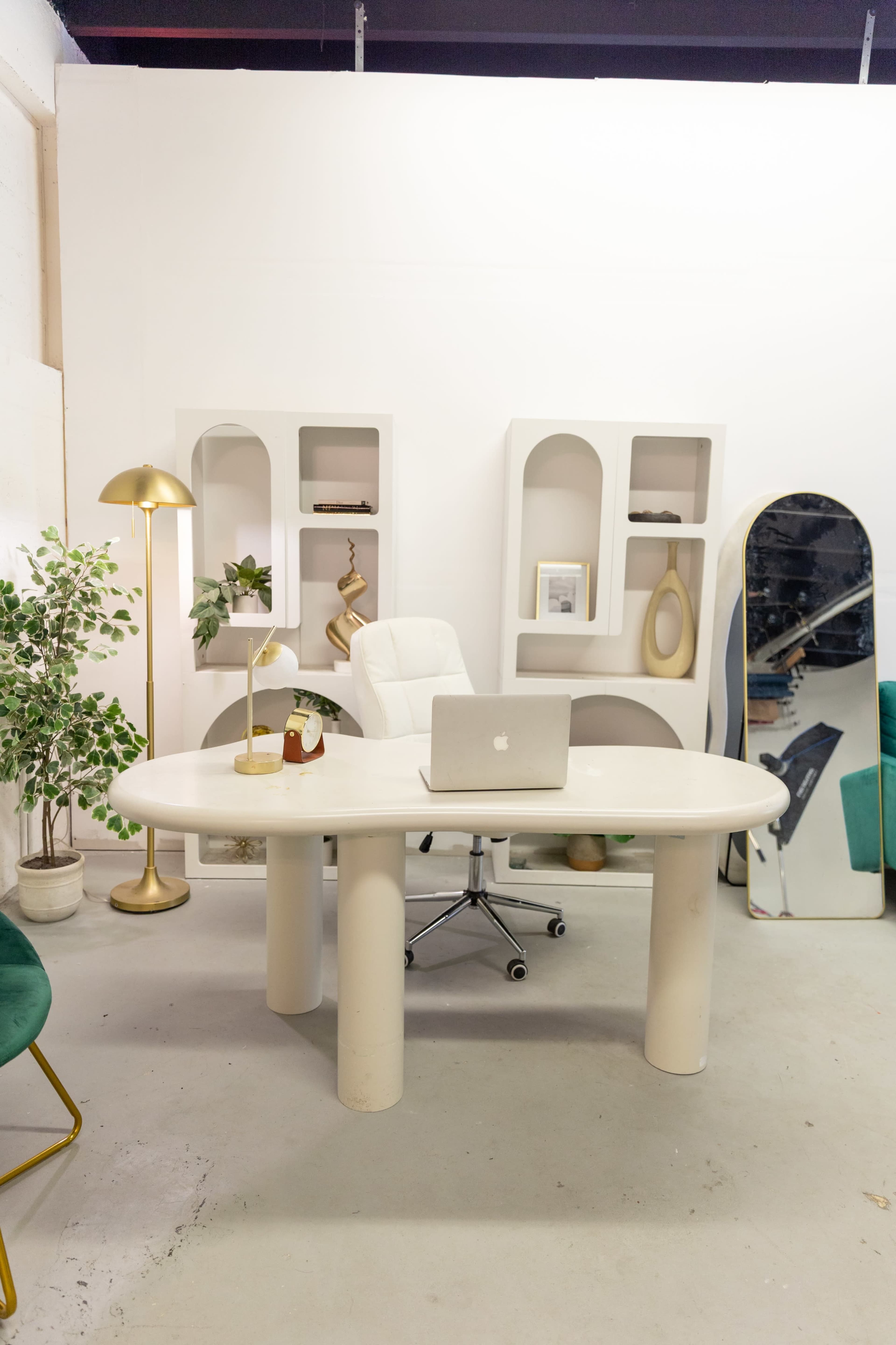 The image showcases a modern office space featuring a white curved desk, an ergonomic chair, and decorative shelves with plants and accessories.