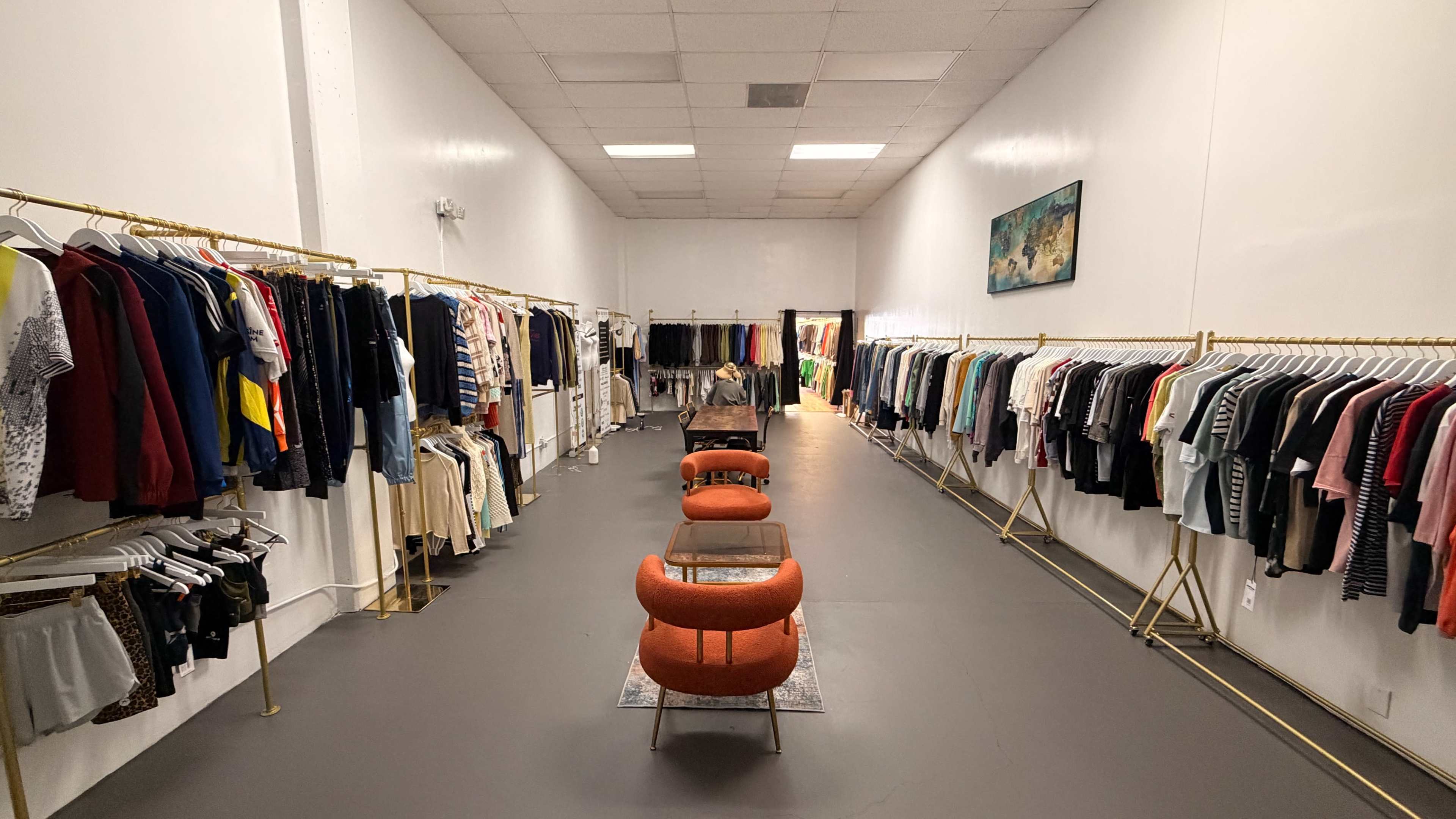 The image shows a clothing store with racks of apparel lining the walls and a seating area in the center.