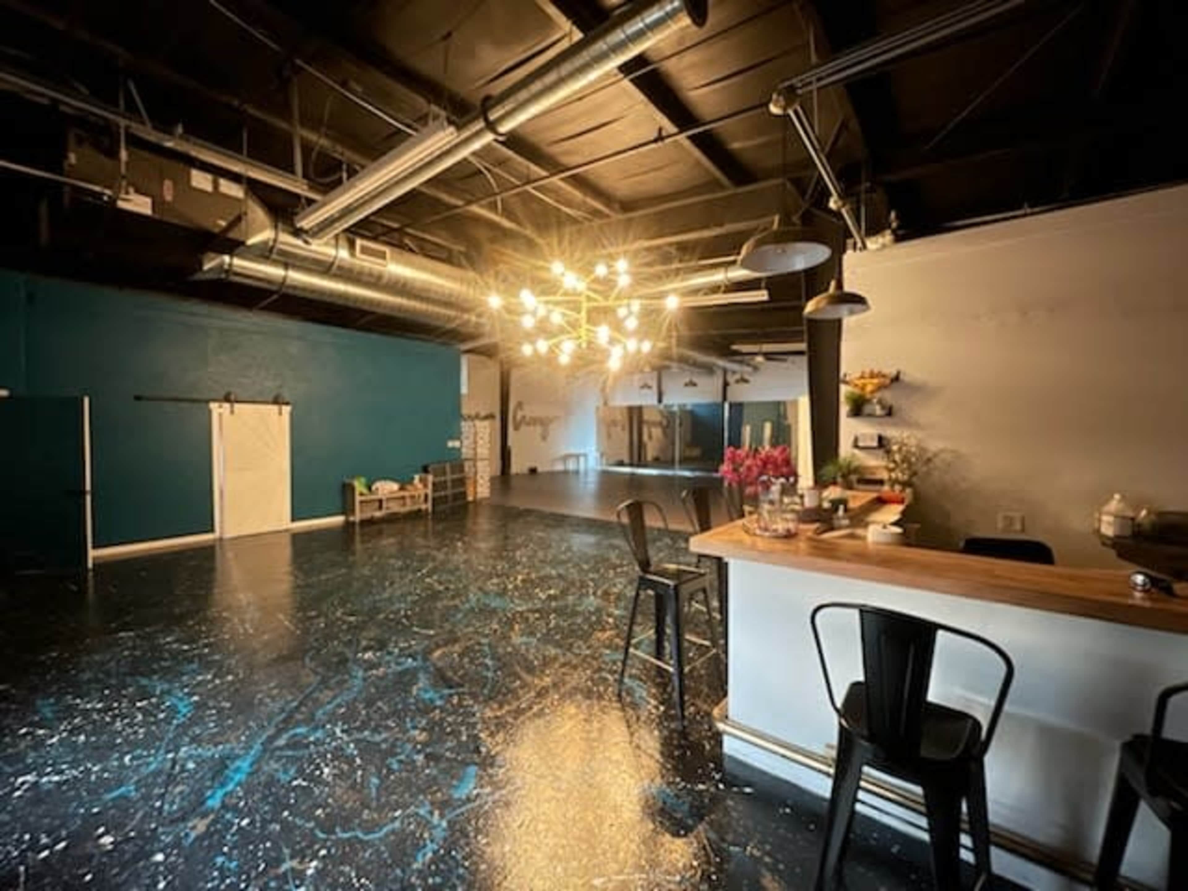 An empty interior space featuring a bar with stools, a blue accent wall, and industrial lighting above.