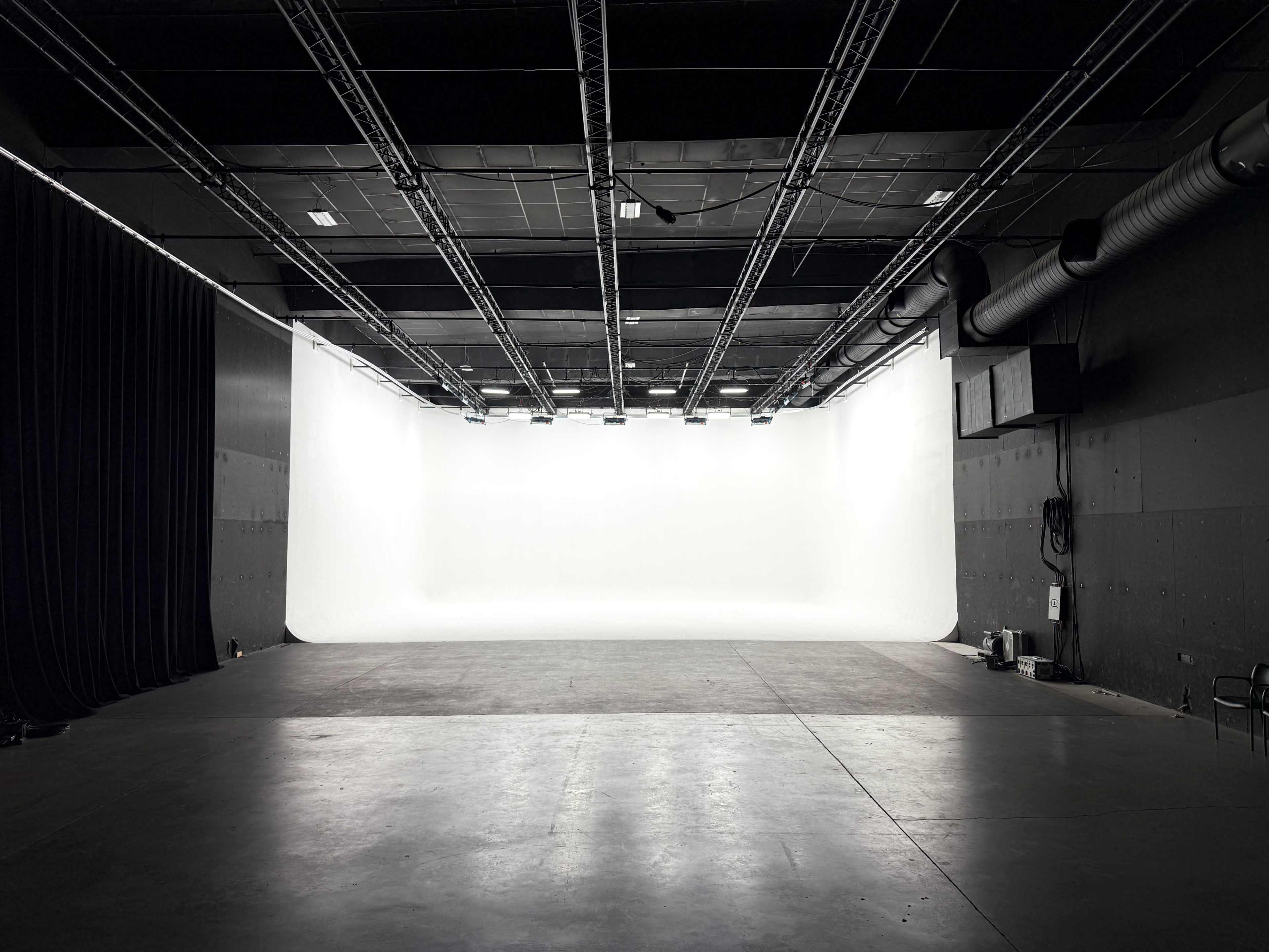 The image depicts a large, empty studio space with a white backdrop and dimmed lighting.