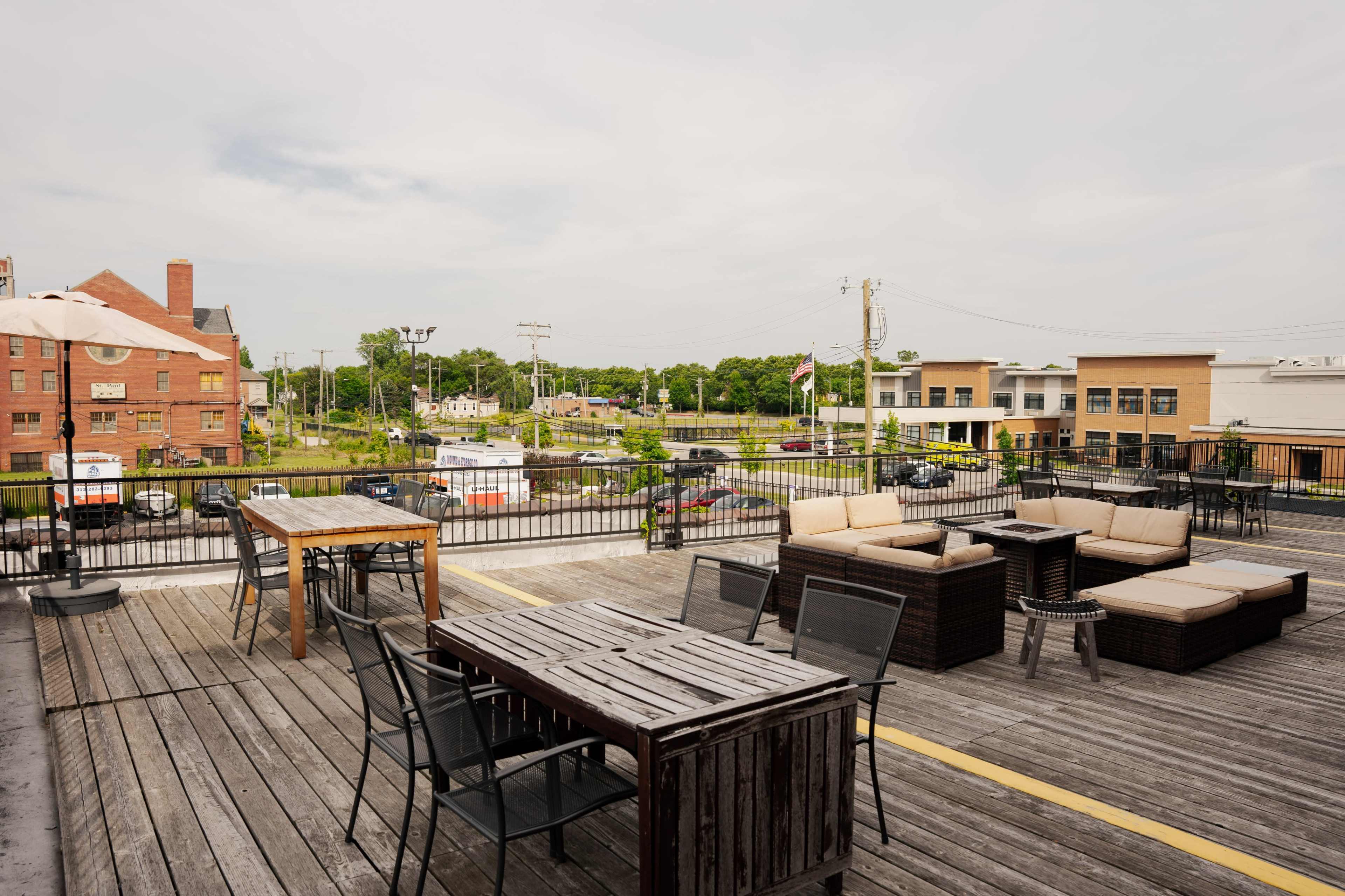 A rooftop patio features wooden furniture and a view of a nearby street and commercial buildings.