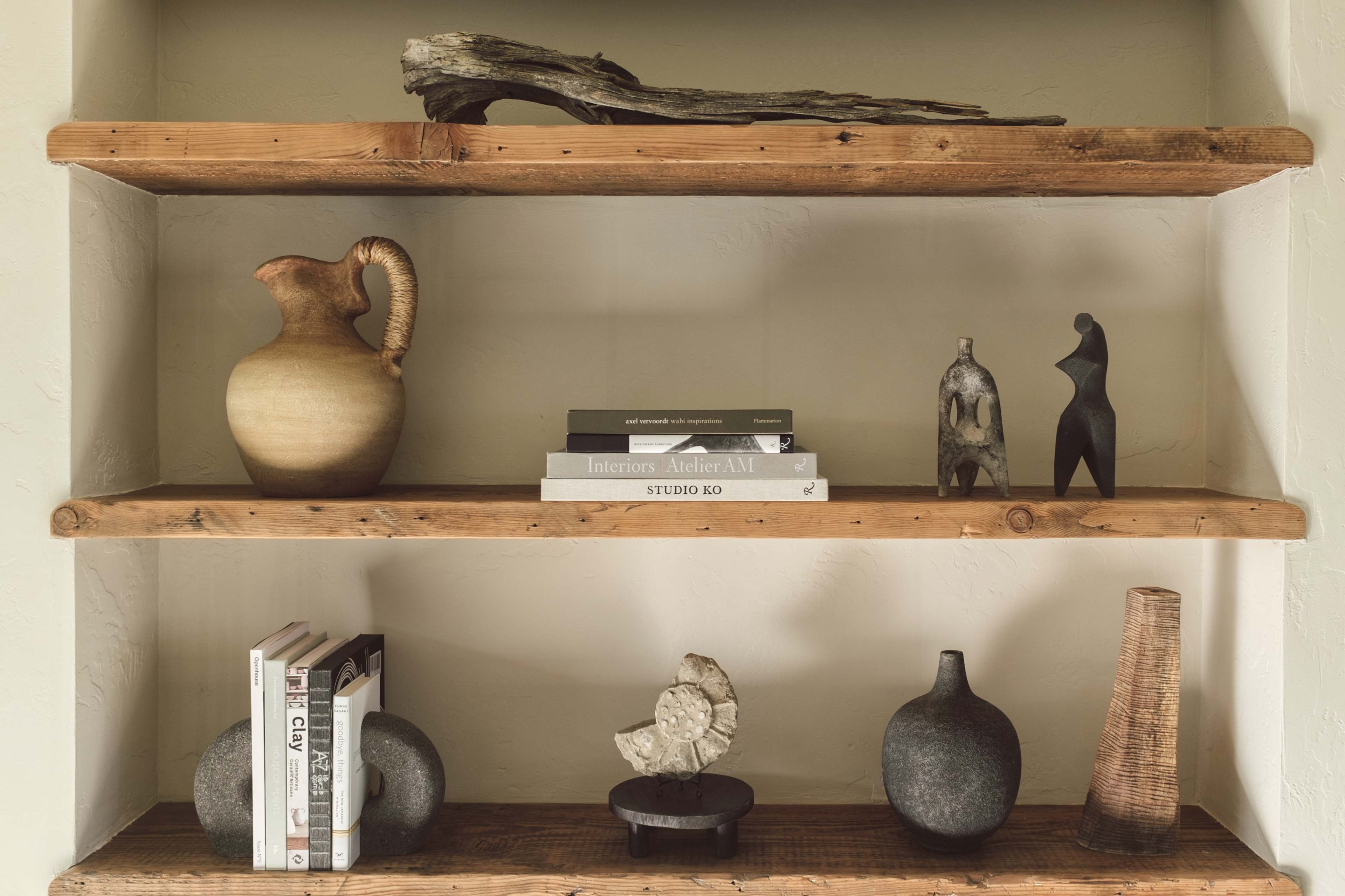 A wooden shelf with three tiers displaying various decorative items, including pottery, books, and sculptures.