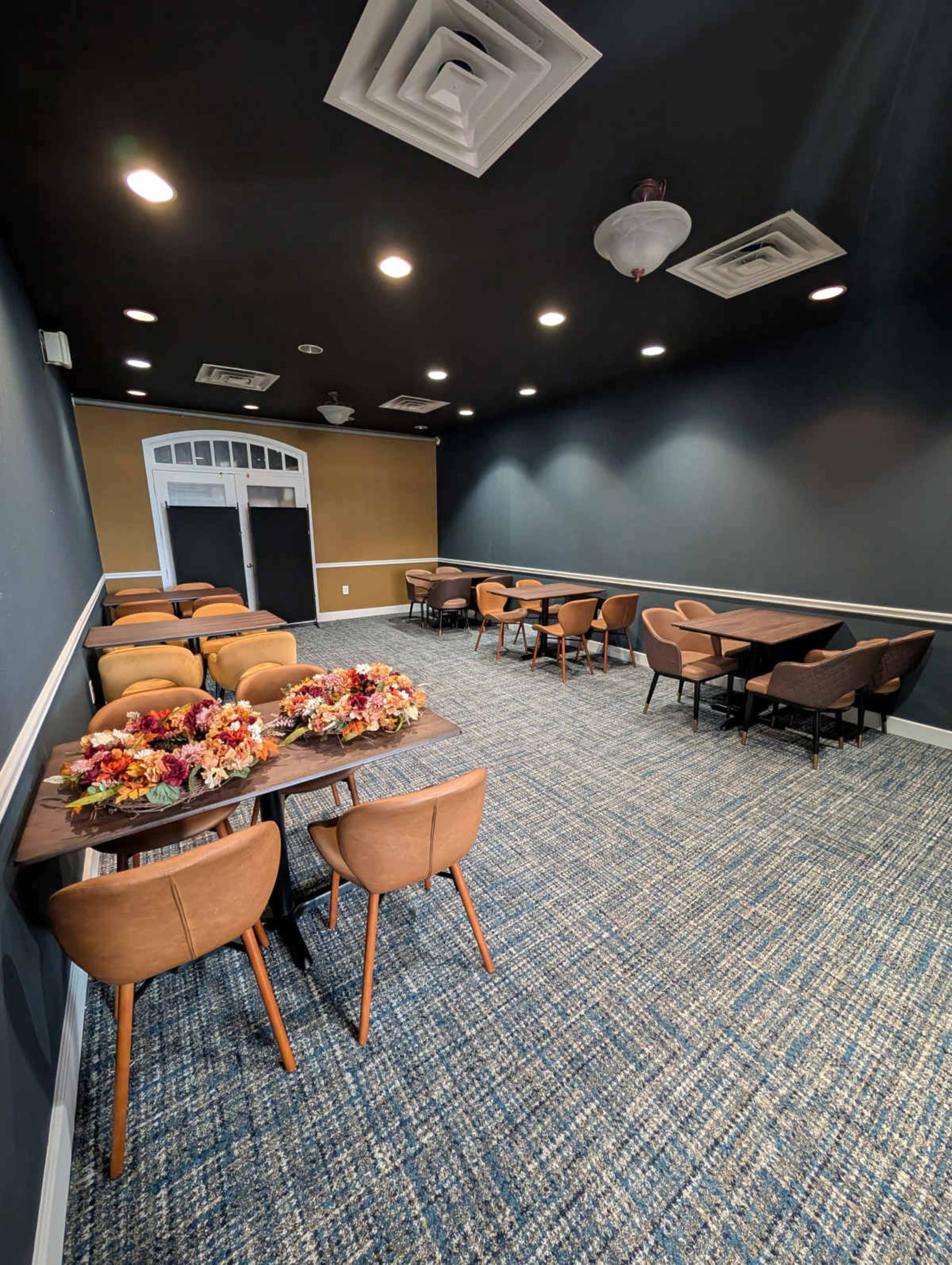 The image shows a spacious meeting room with multiple tables and chairs arranged neatly, decorated with a floral centerpiece on one table.