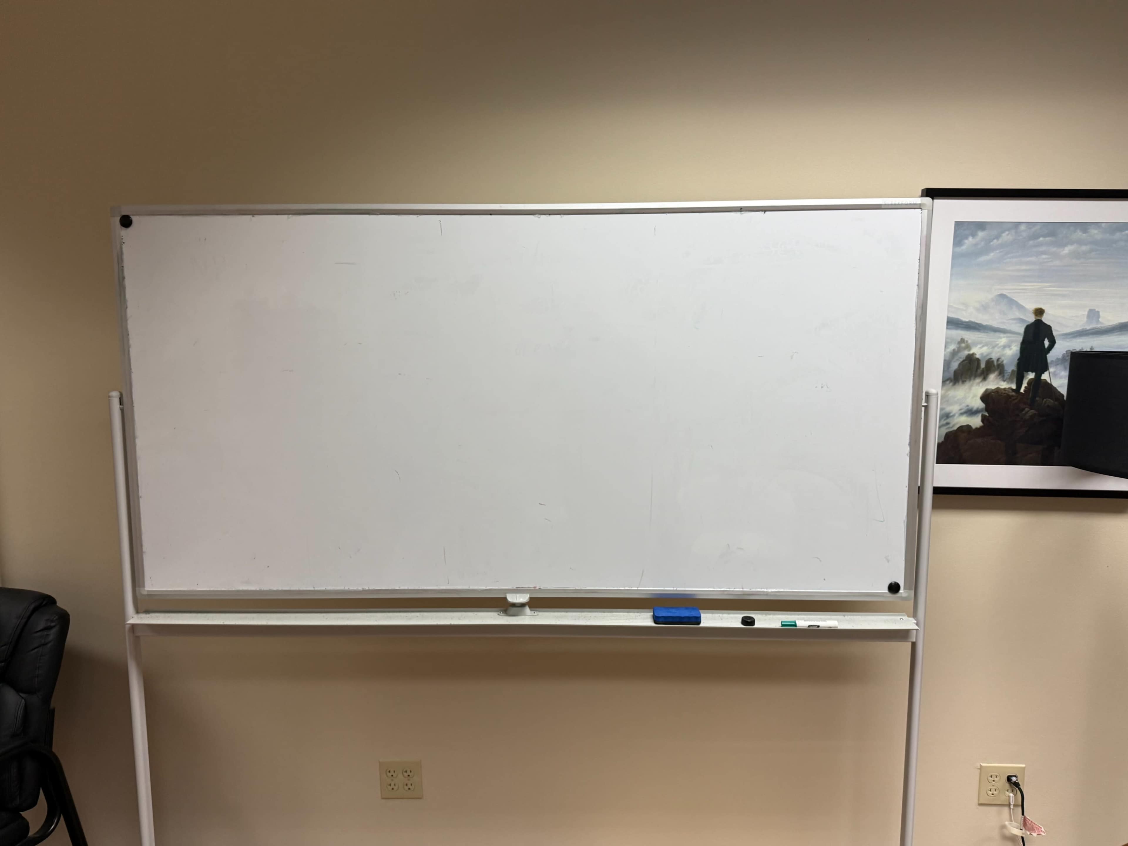 The image shows a blank whiteboard in an office setting, with a chair to the left and a framed picture on the wall behind.