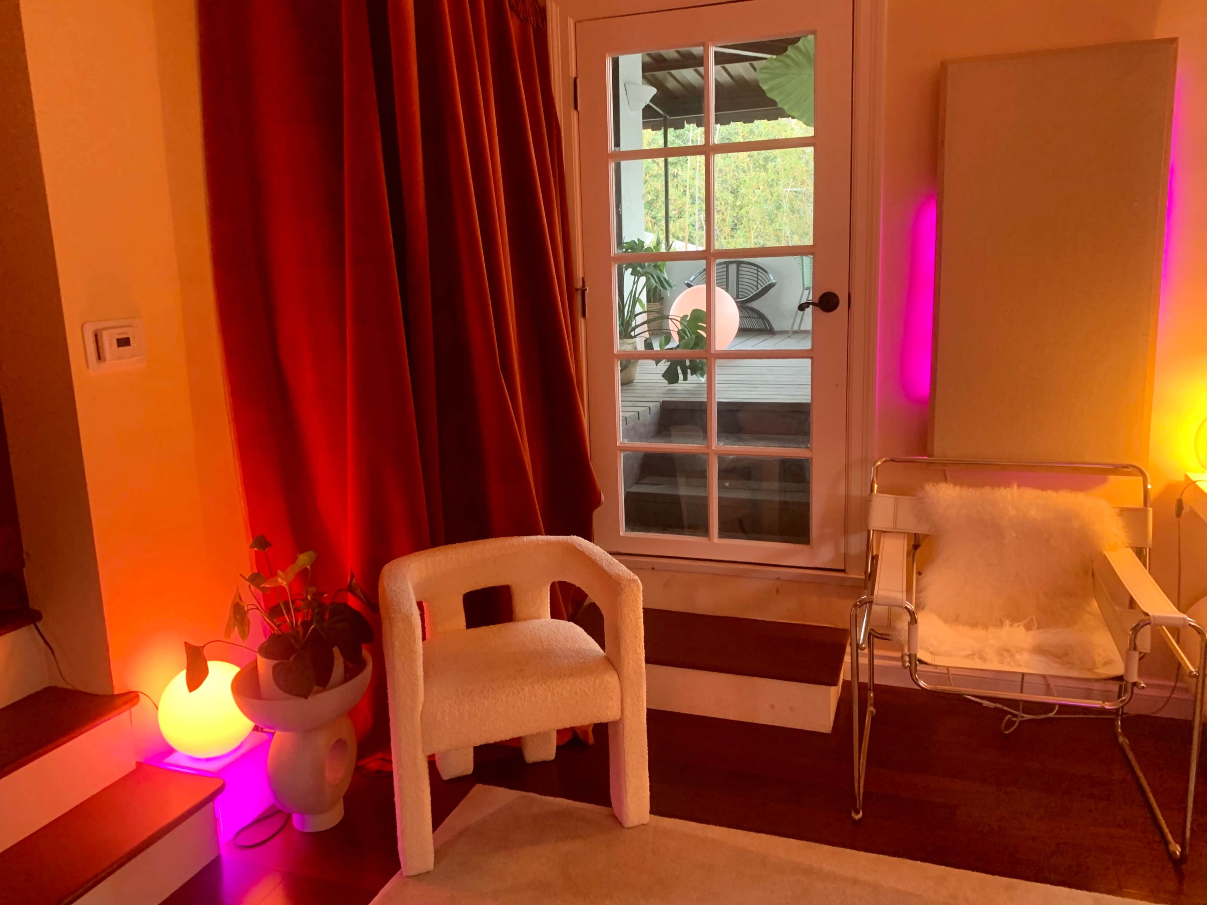The scene features a cozy room with a red curtain, a white chair, and a glass door leading to an outdoor space, illuminated by soft lighting.
