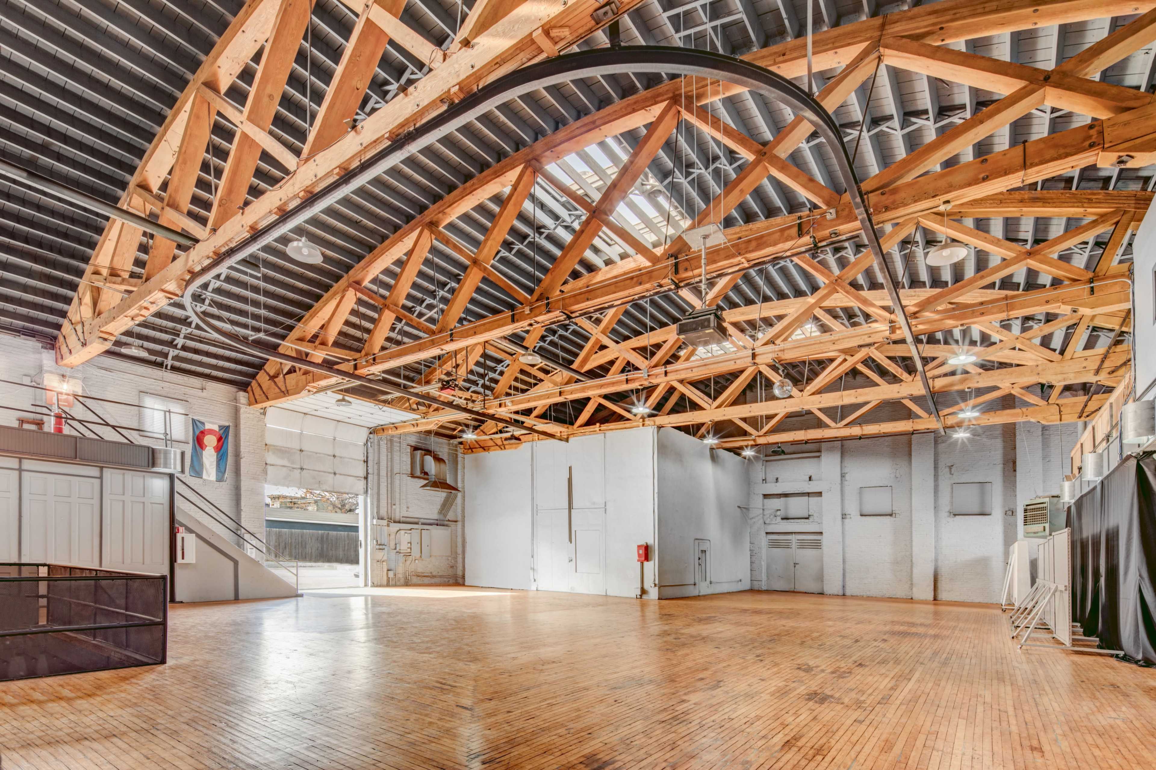 A spacious interior with wooden beams, polished wooden flooring, and multiple large windows allowing natural light to enter.