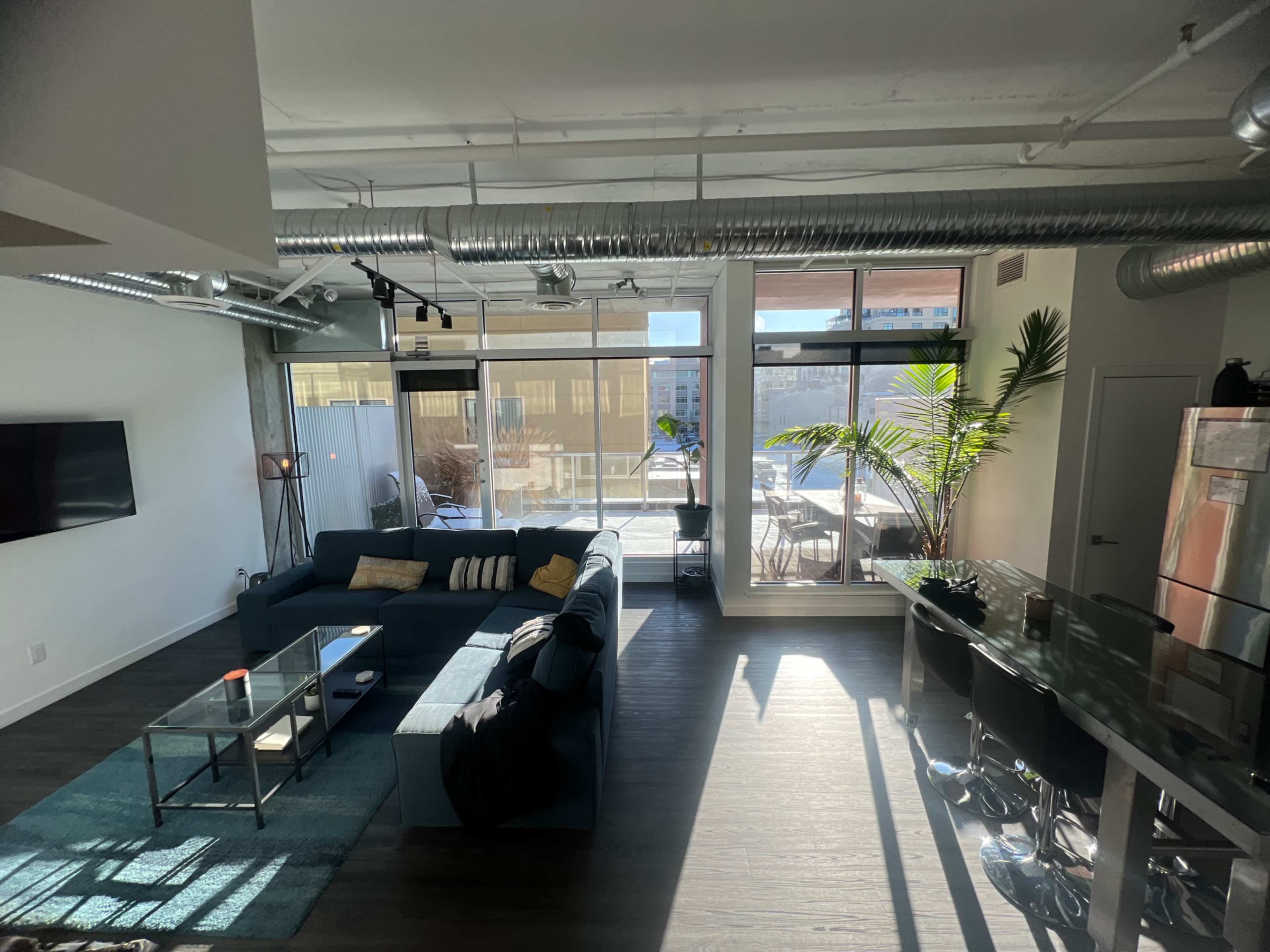 A spacious, modern living area features a sectional sofa, a glass coffee table, and large windows that offer a view of an outdoor patio.