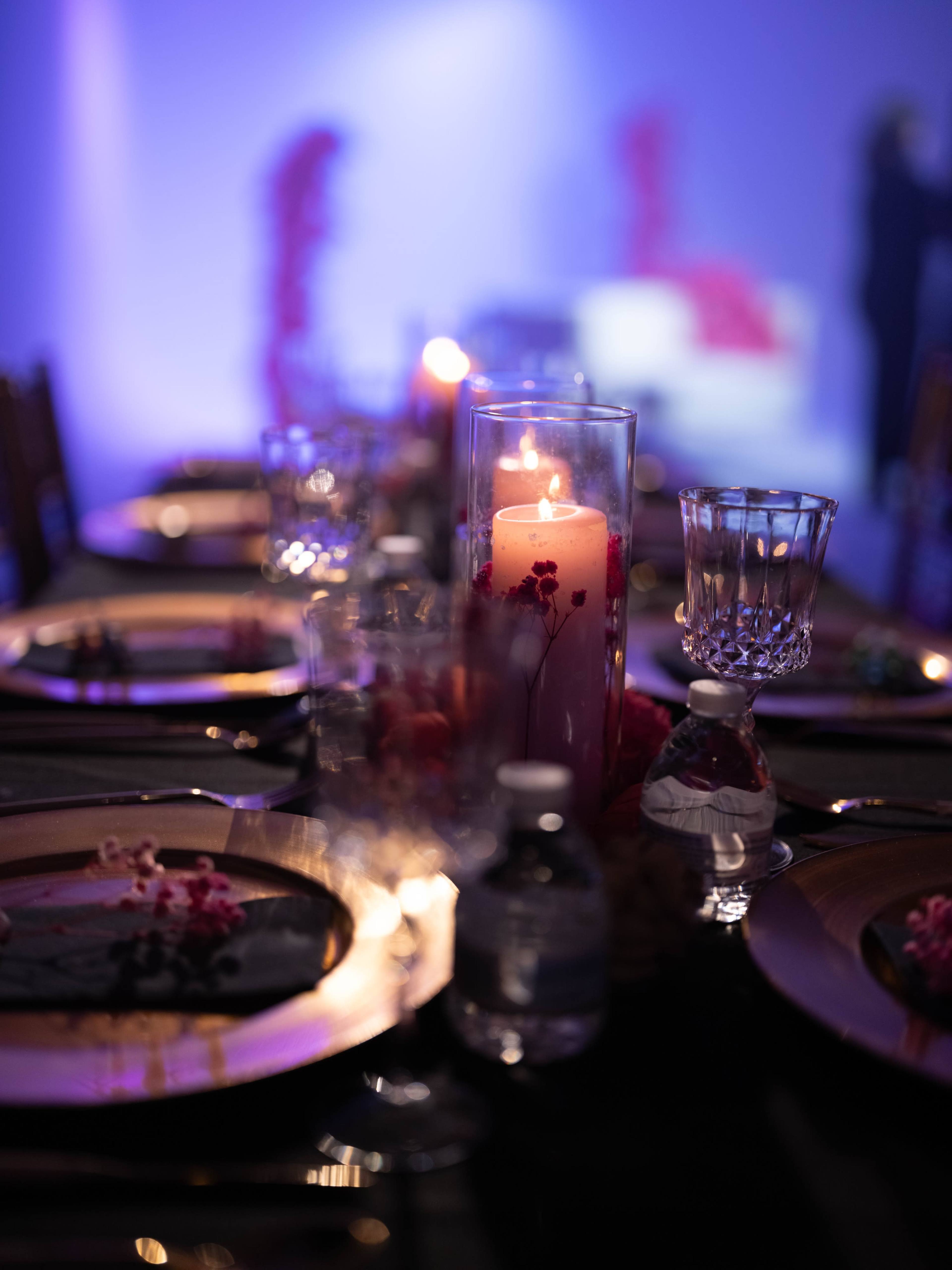 A table is elegantly set with lit candles, decorative elements, and water bottles against a softly lit background.