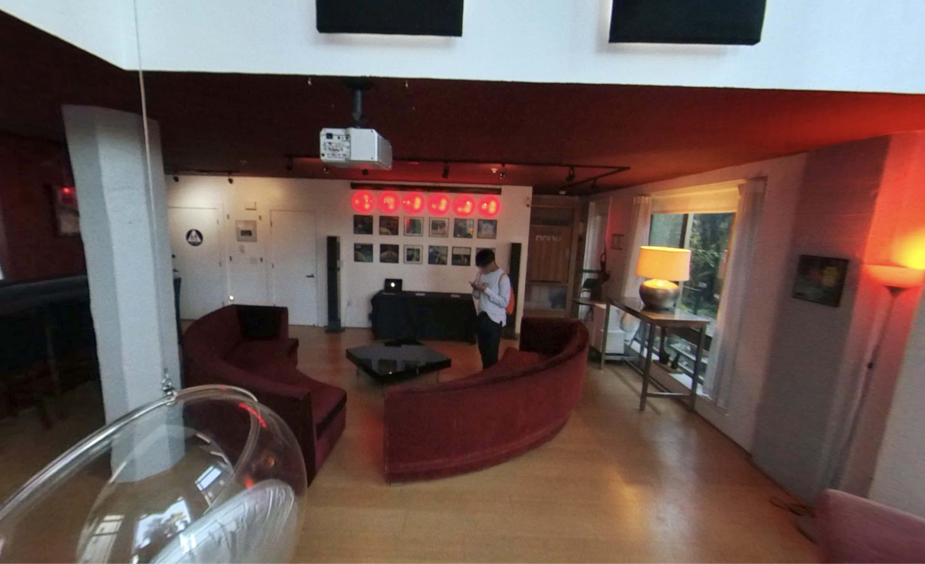 A modern interior with two red sofas arranged in a semi-circle around a low black table, along with a projector, framed photos on the wall, and a lamp.