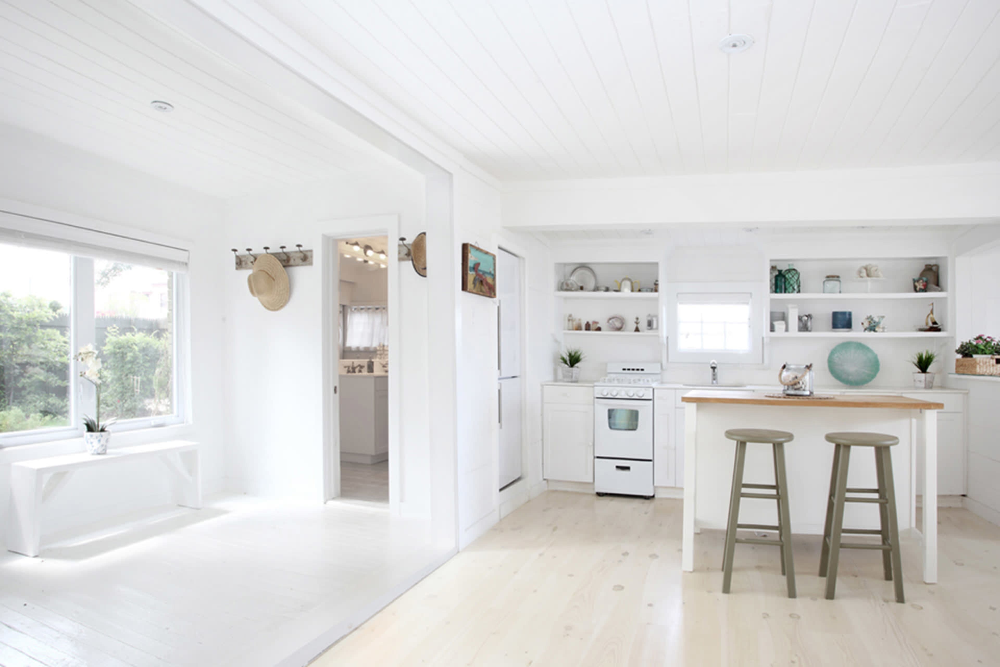 A bright, minimalist kitchen with white walls, a wooden island, and shelves displaying decorative items.