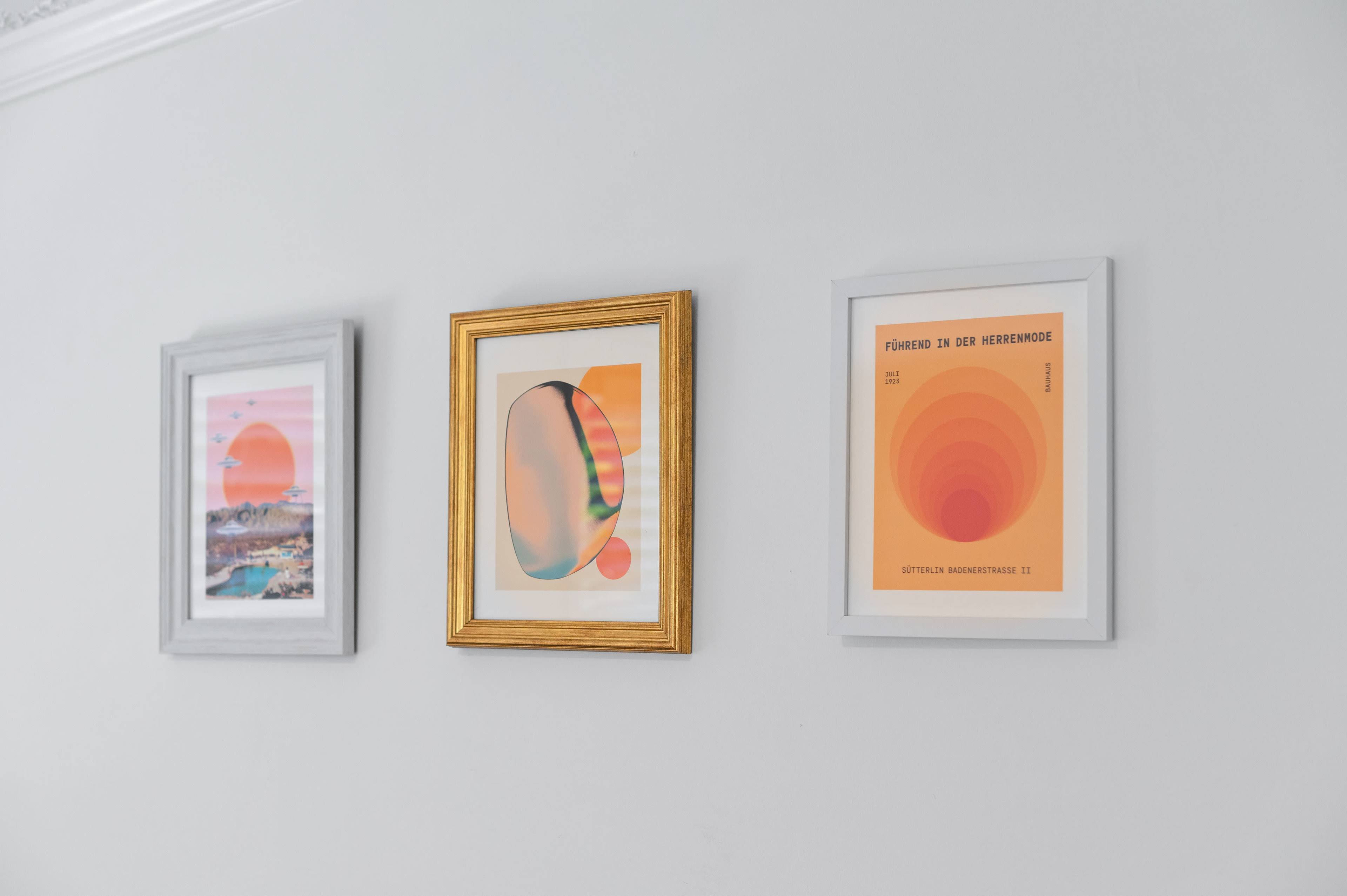 Three framed art prints with vibrant colors are hanging on a light-colored wall.