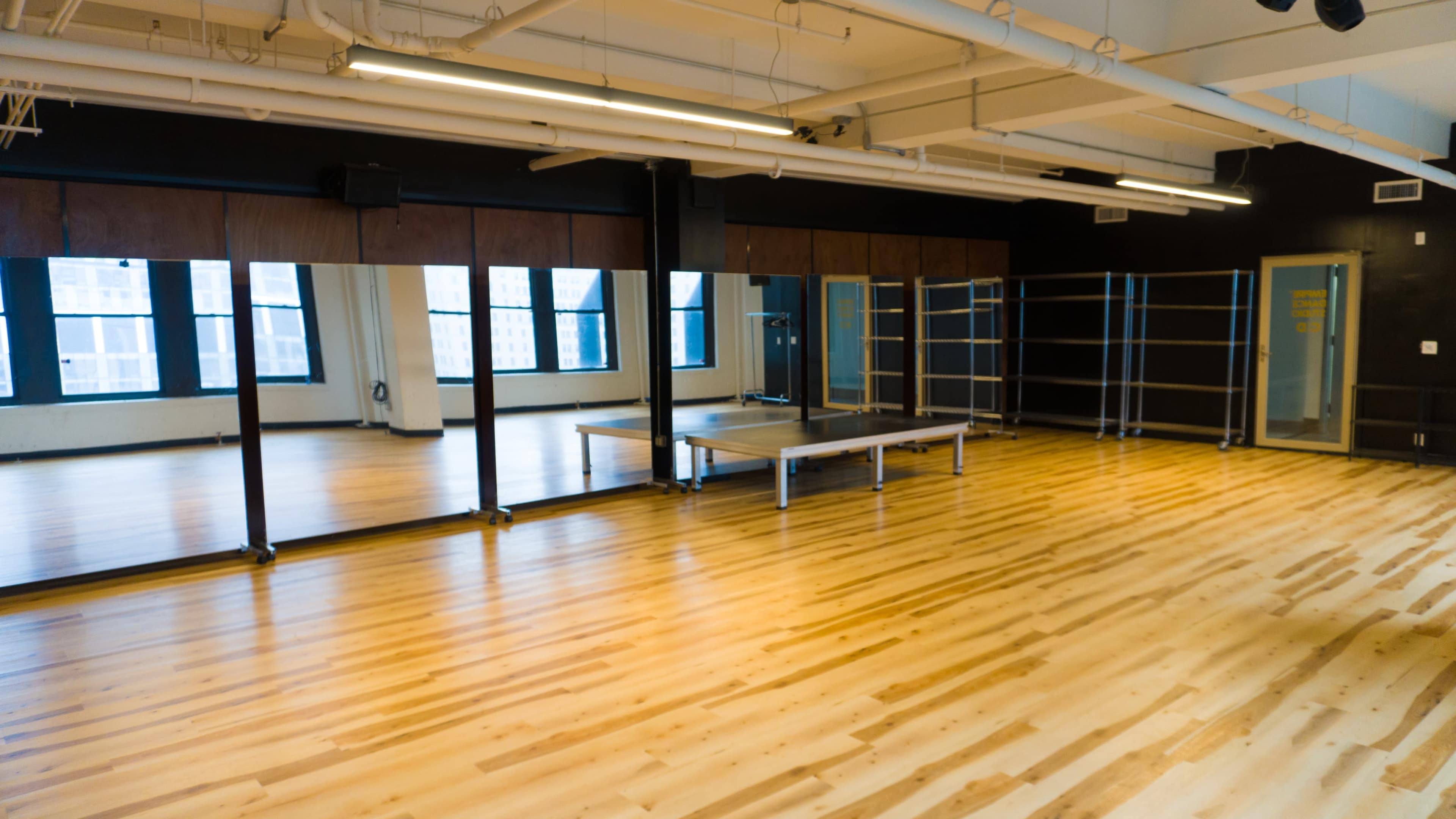 The image shows a spacious, empty interior of a dance studio with wooden flooring and large mirrors on one wall.