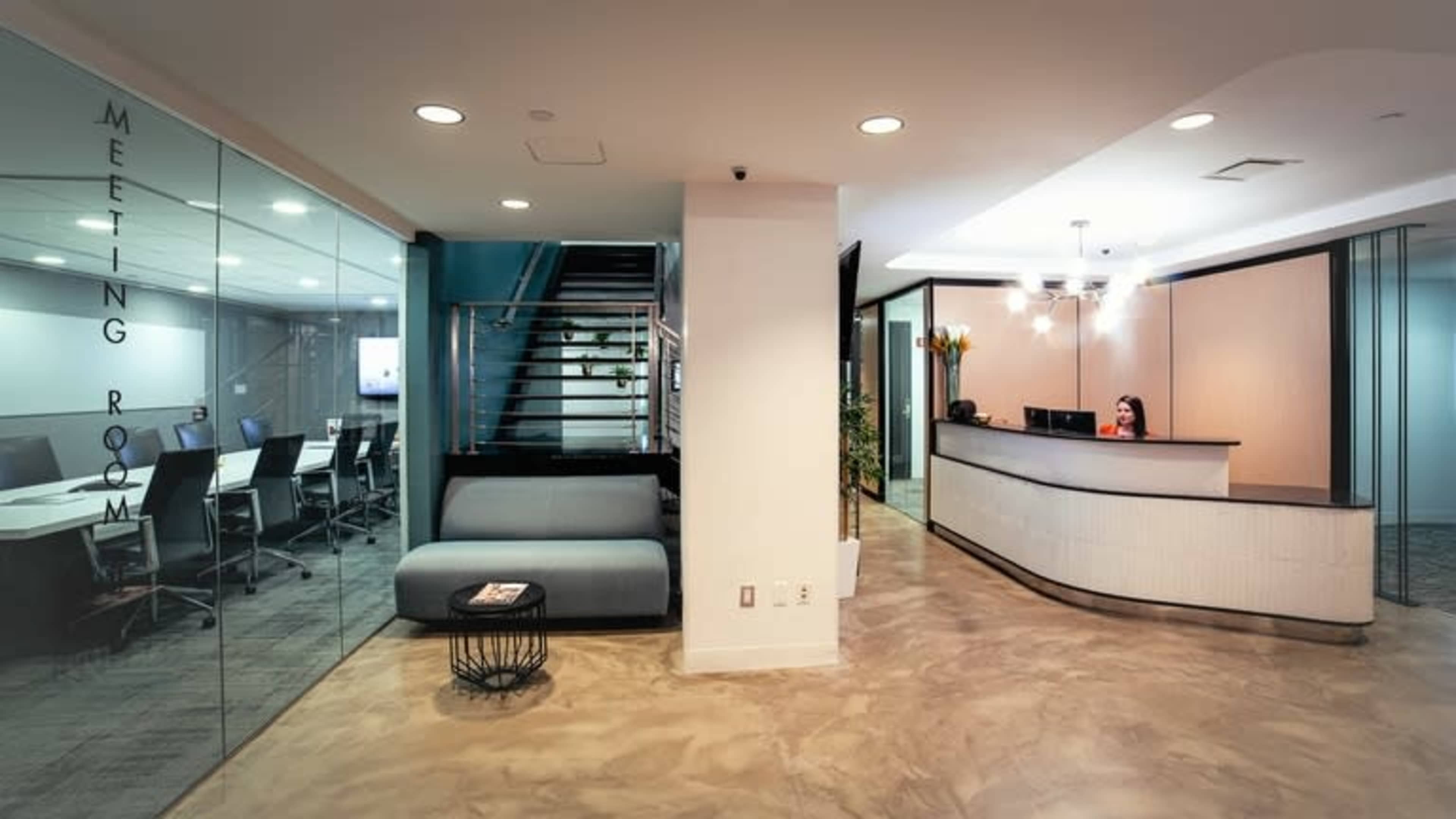 A modern office reception area with a front desk, a waiting area, and a glass-walled meeting room visible in the background.