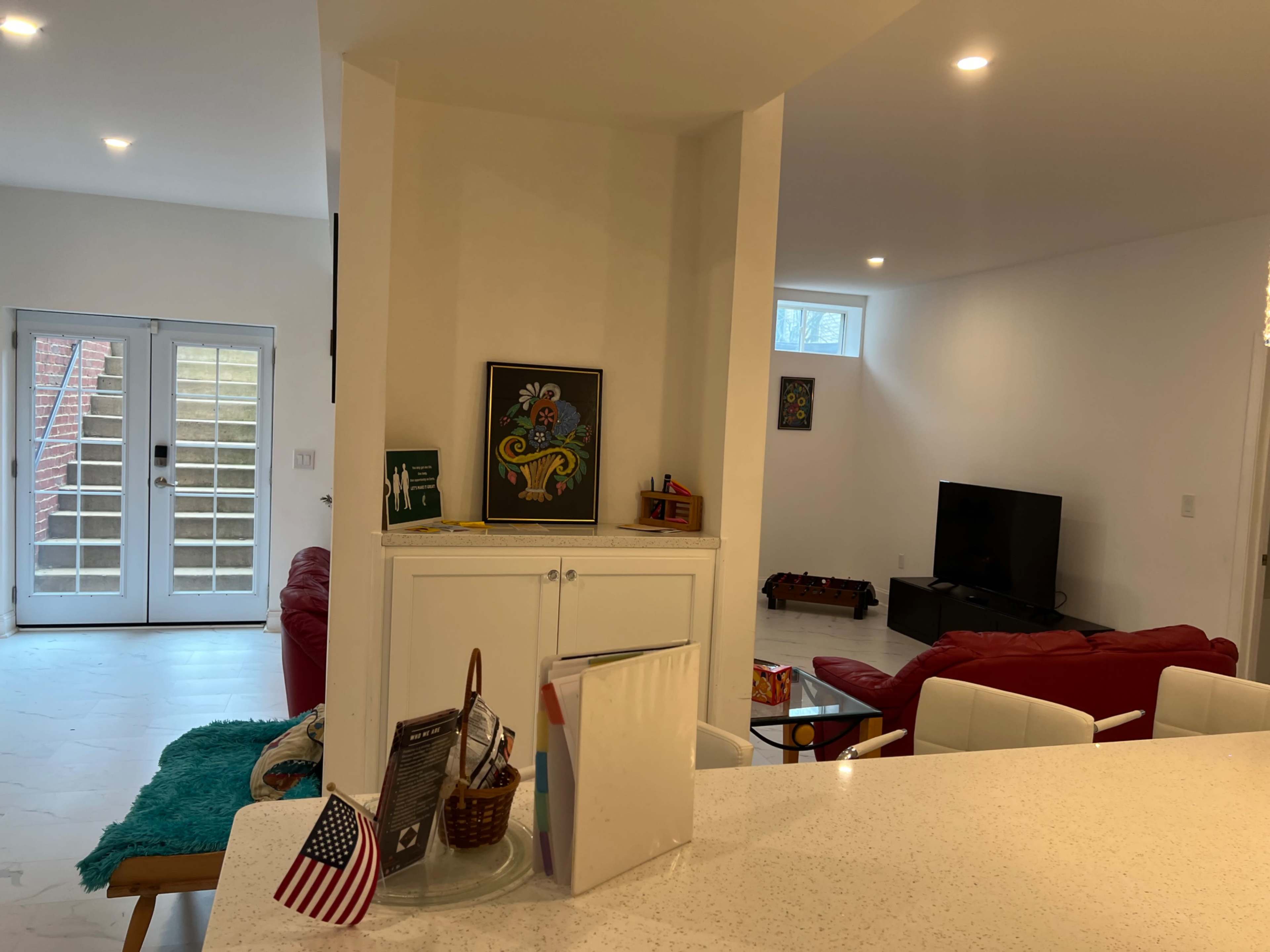 The image shows a modern living space with a kitchen island facing a lounge area, featuring red sofas and a television.