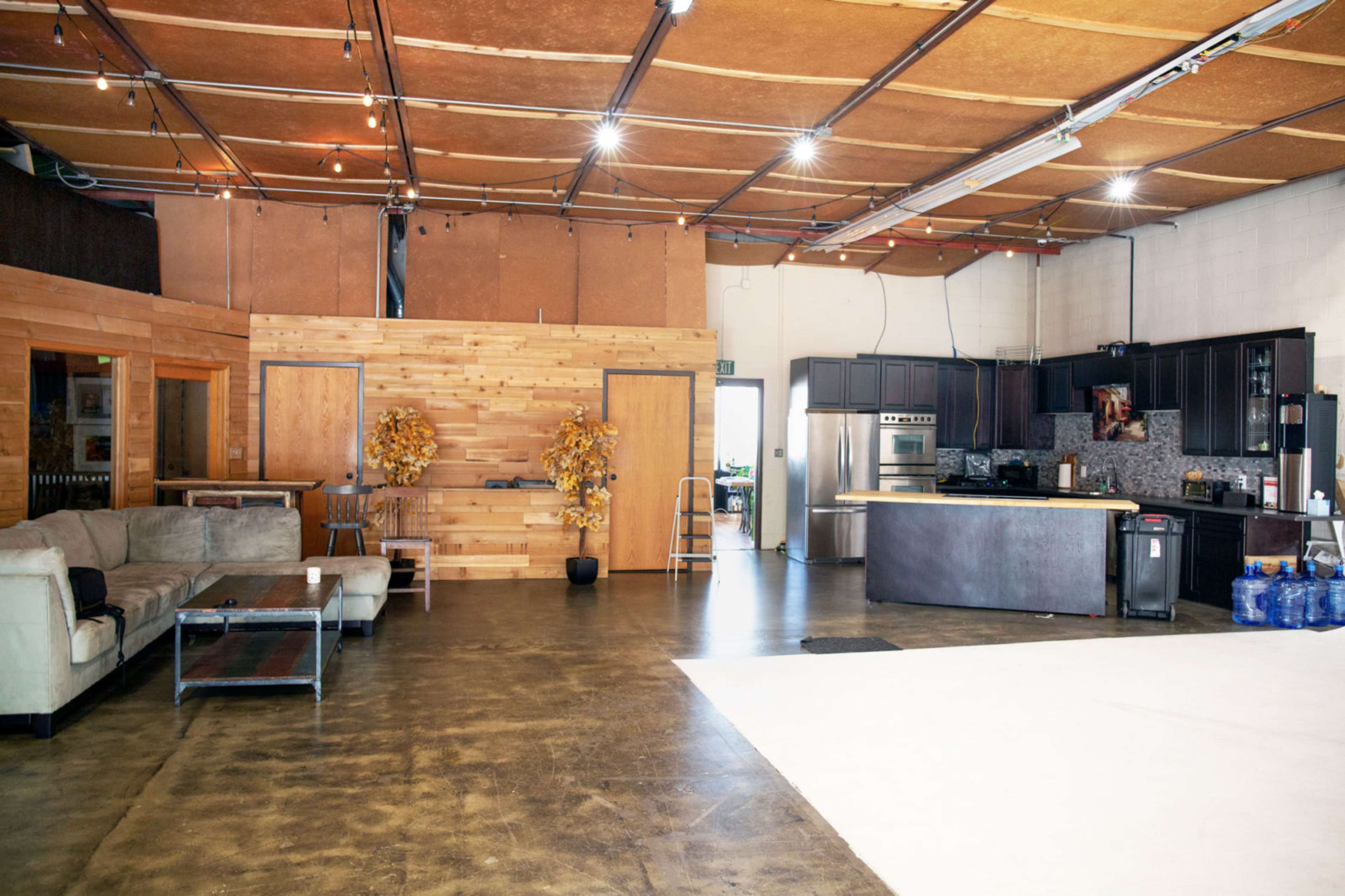 A spacious, industrial-style interior with exposed ceilings, a kitchen area, and a seating arrangement made of a couch and a coffee table.