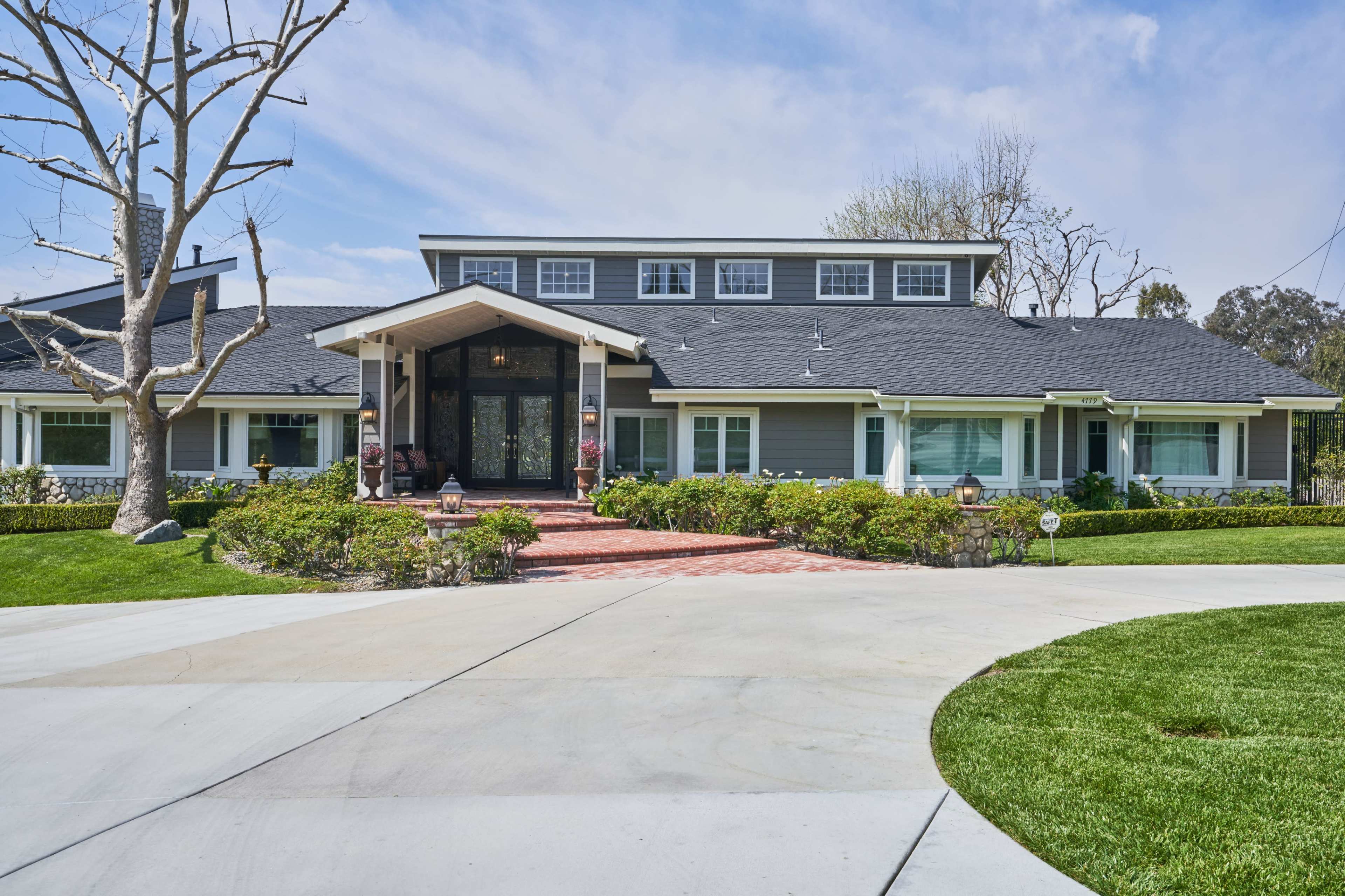 A large, modern house with a distinctive peaked entrance and a circular driveway surrounded by well-maintained landscaping.