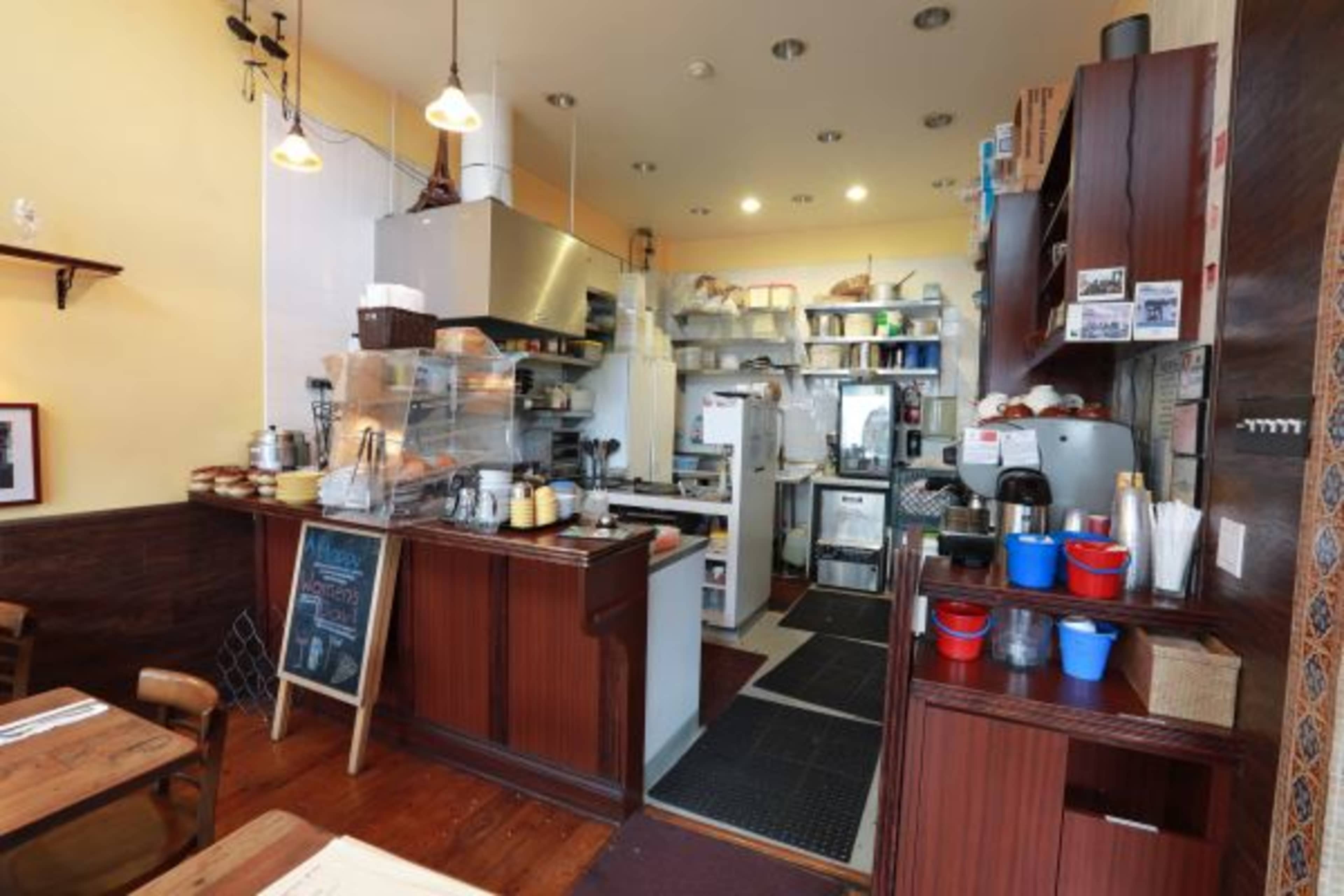 A small café interior with a countertop, coffee machines, and shelves filled with kitchen supplies.