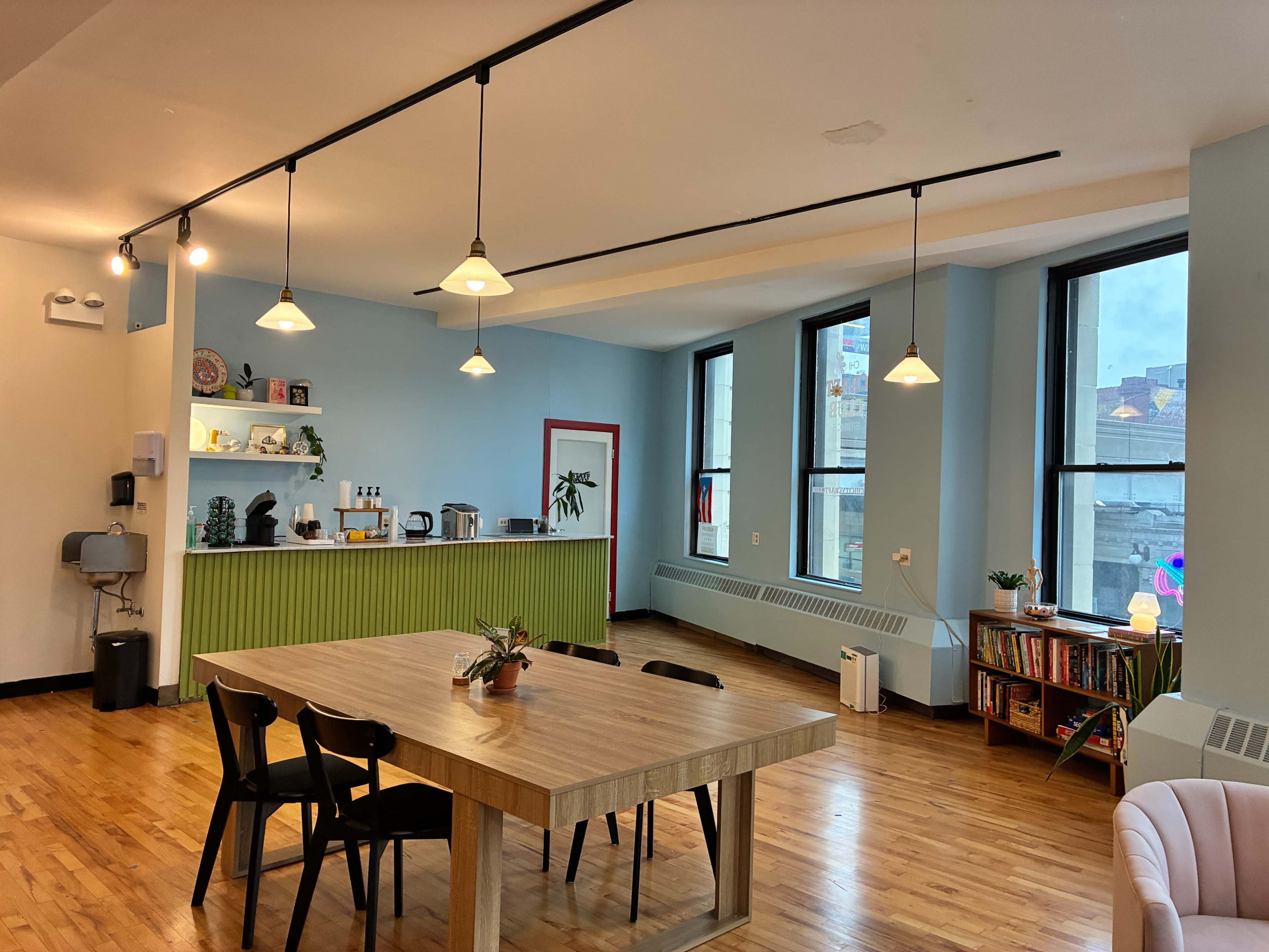 The image shows a modern kitchen and dining area with a wooden table, black chairs, and large windows allowing natural light.