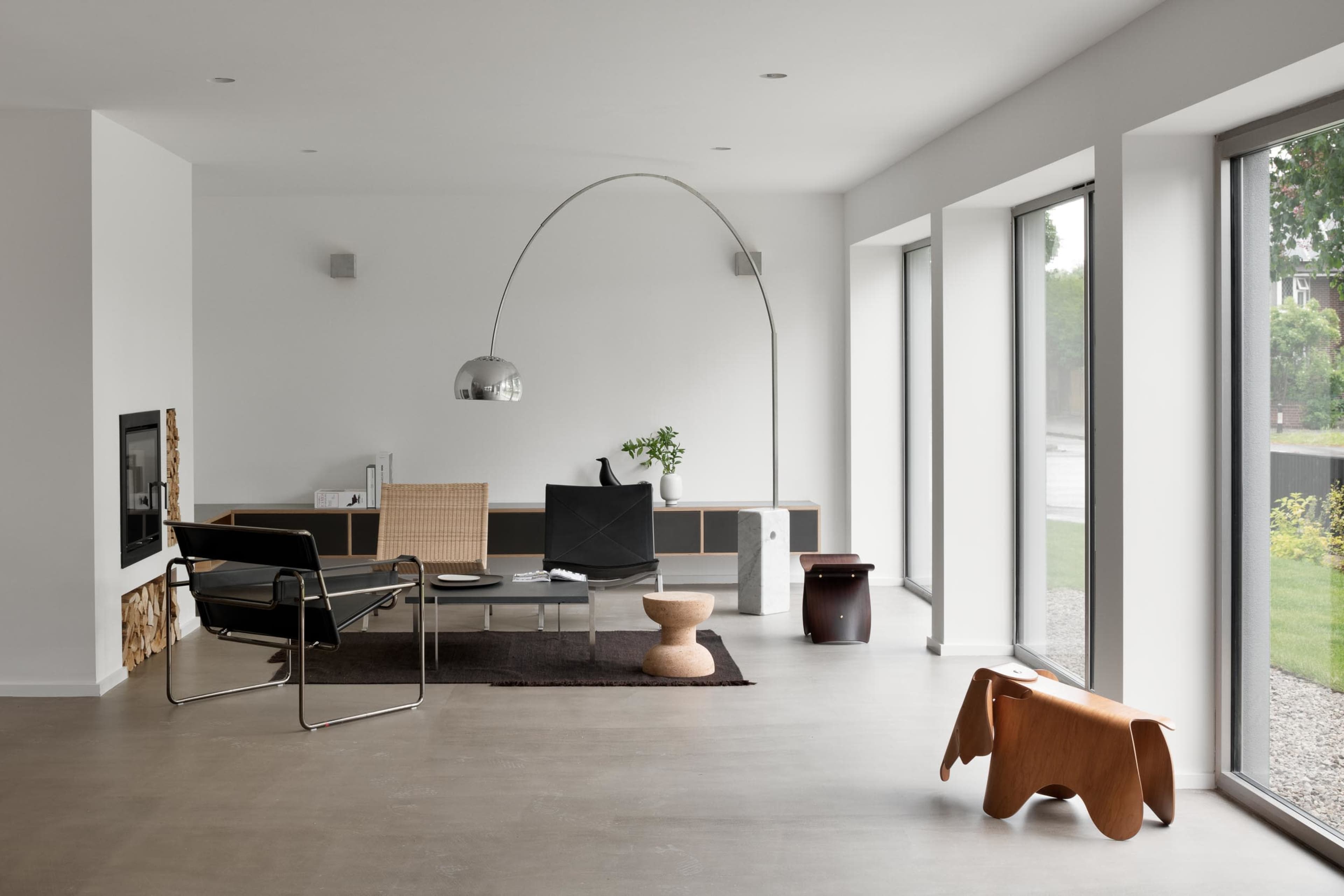 A modern living room with minimalist furniture, including a sleek chair, a coffee table, and large windows allowing natural light to fill the space.