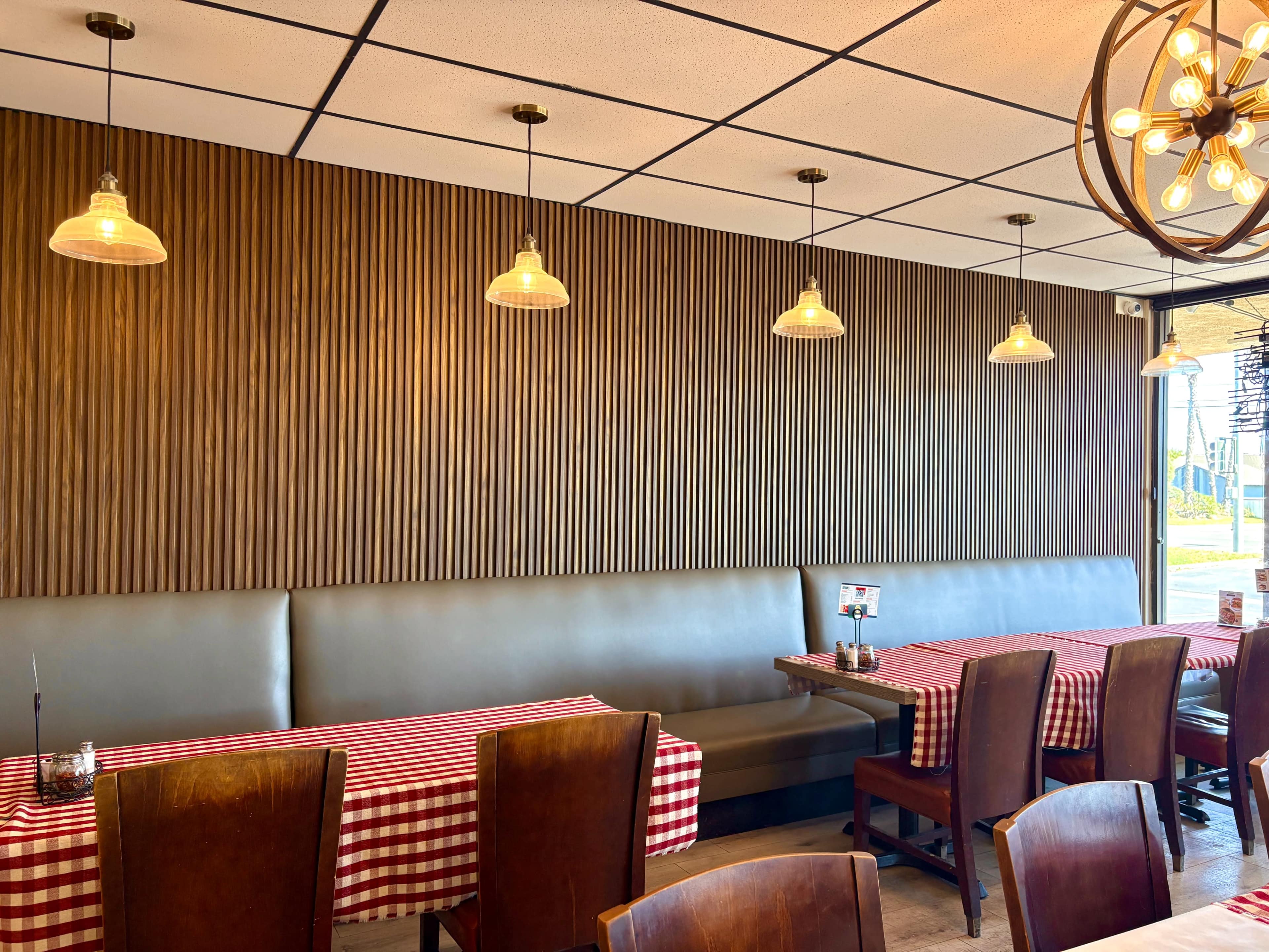 The image shows a restaurant interior with wooden paneling and red-and-white checkered tablecloths on the tables, accompanied by pendant lighting.