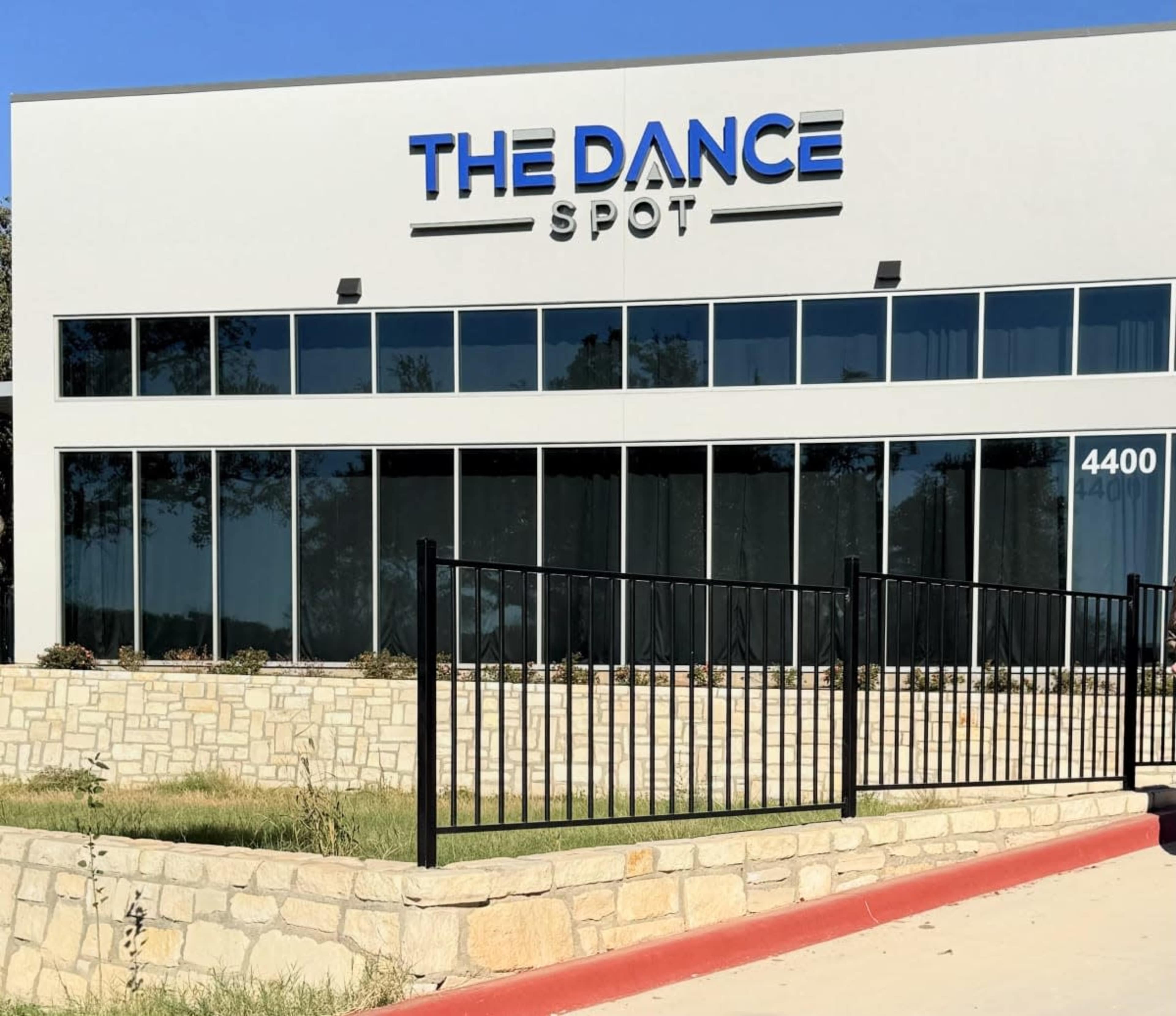 The image shows a modern building labeled "THE DANCE SPOT" with large glass windows and a stone landscaping area in front.