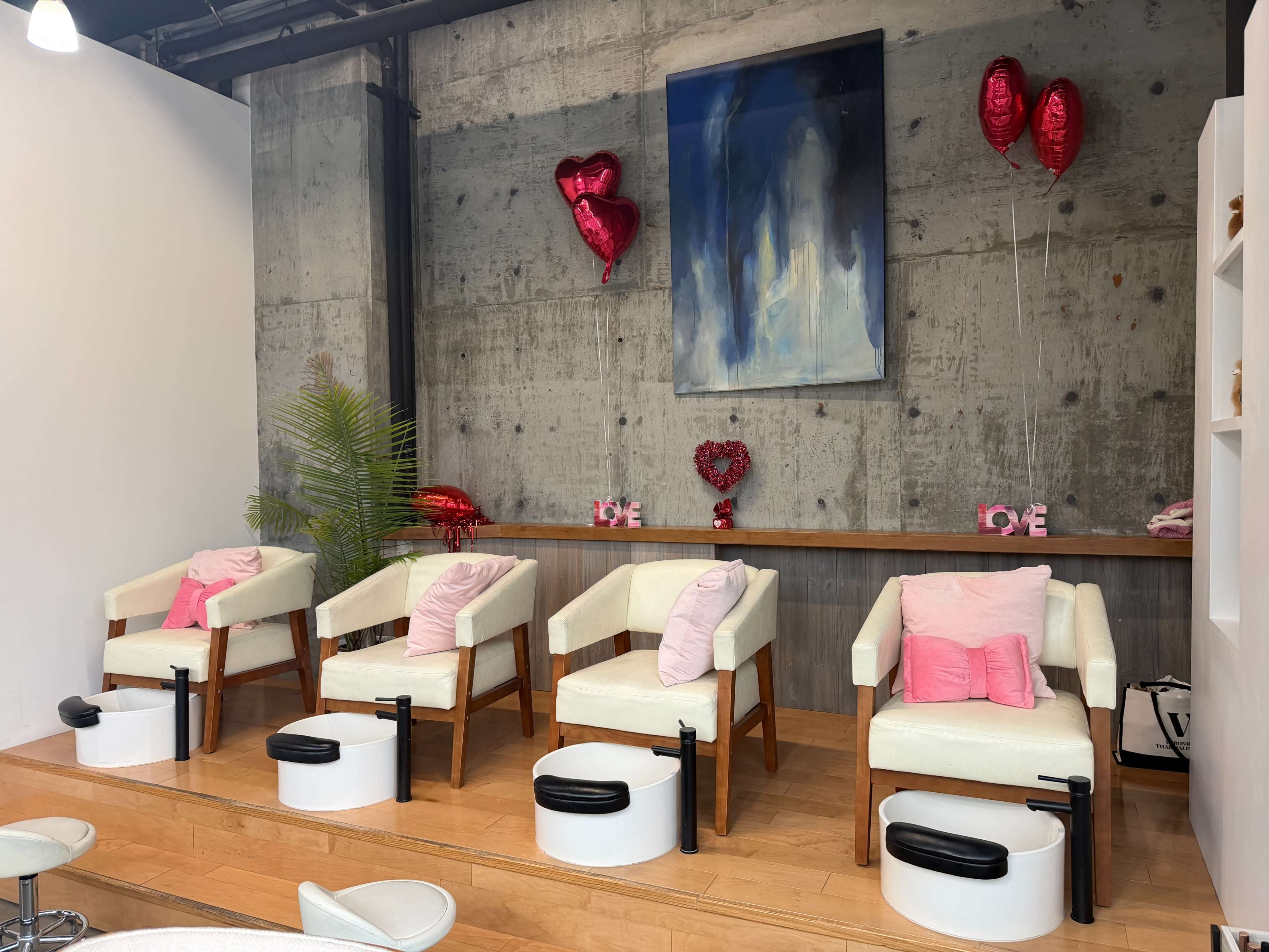 The image shows a modern salon interior with four upholstered chairs, pink cushions, heart-shaped balloons, and a decorative wall painting.
