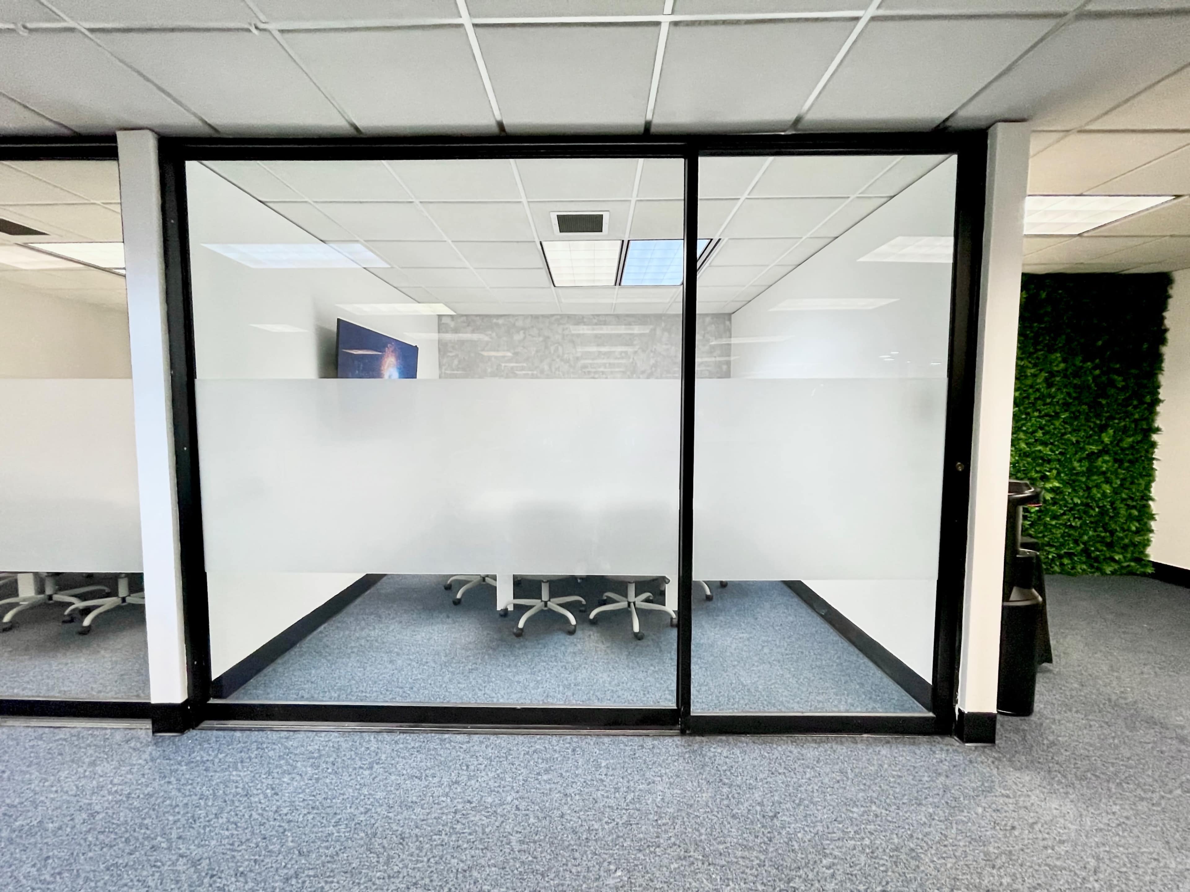 The image shows a glass-walled conference room with a table and chairs inside, partially obscured by frosted glass.
