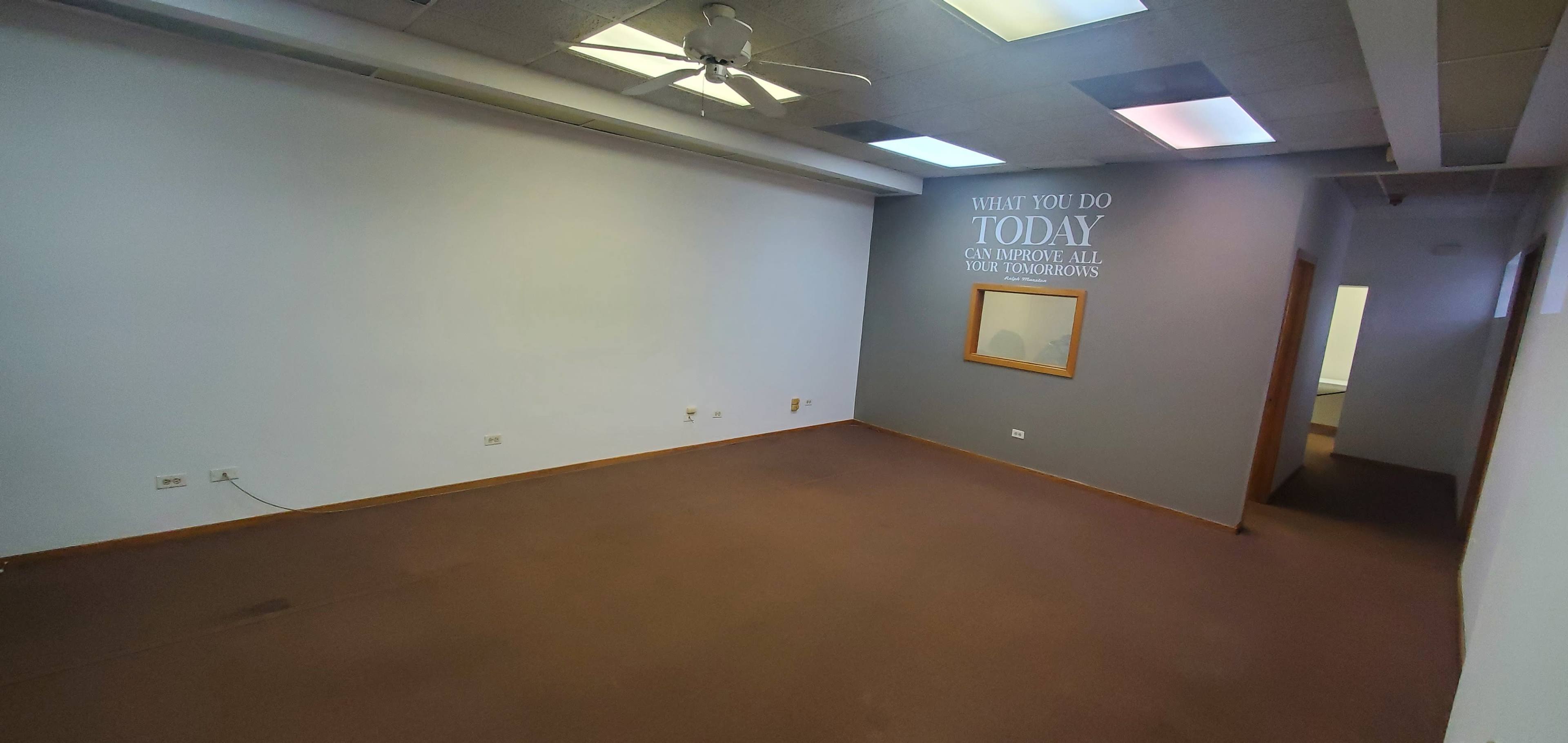 An empty office space with a ceiling fan, two-tone walls, and a framed mirror on one side.