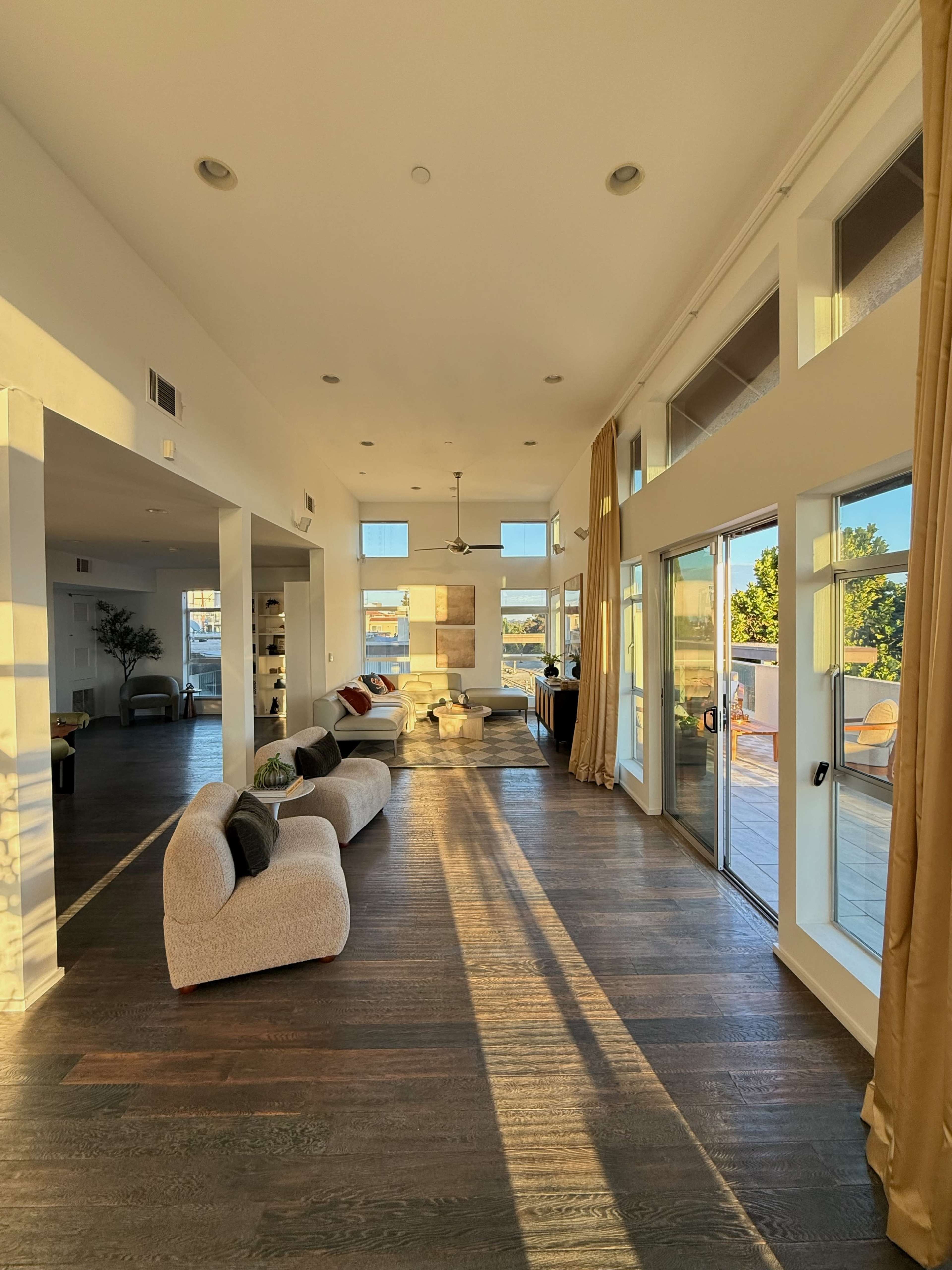A spacious living room features large windows, wooden flooring, and modern furniture.