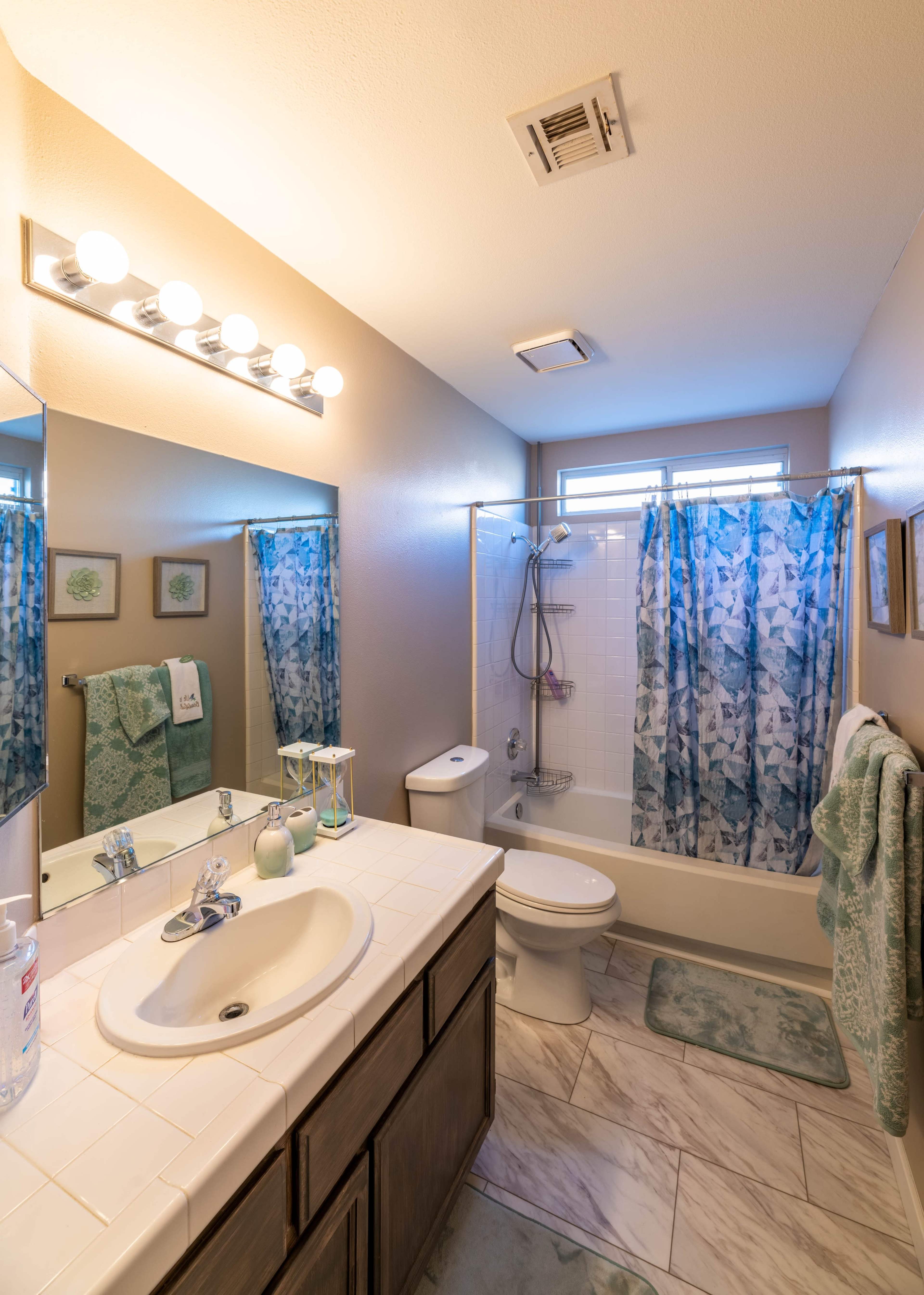 A bathroom with a shower, sink, and toilet, featuring blue and white patterned curtains and towels.