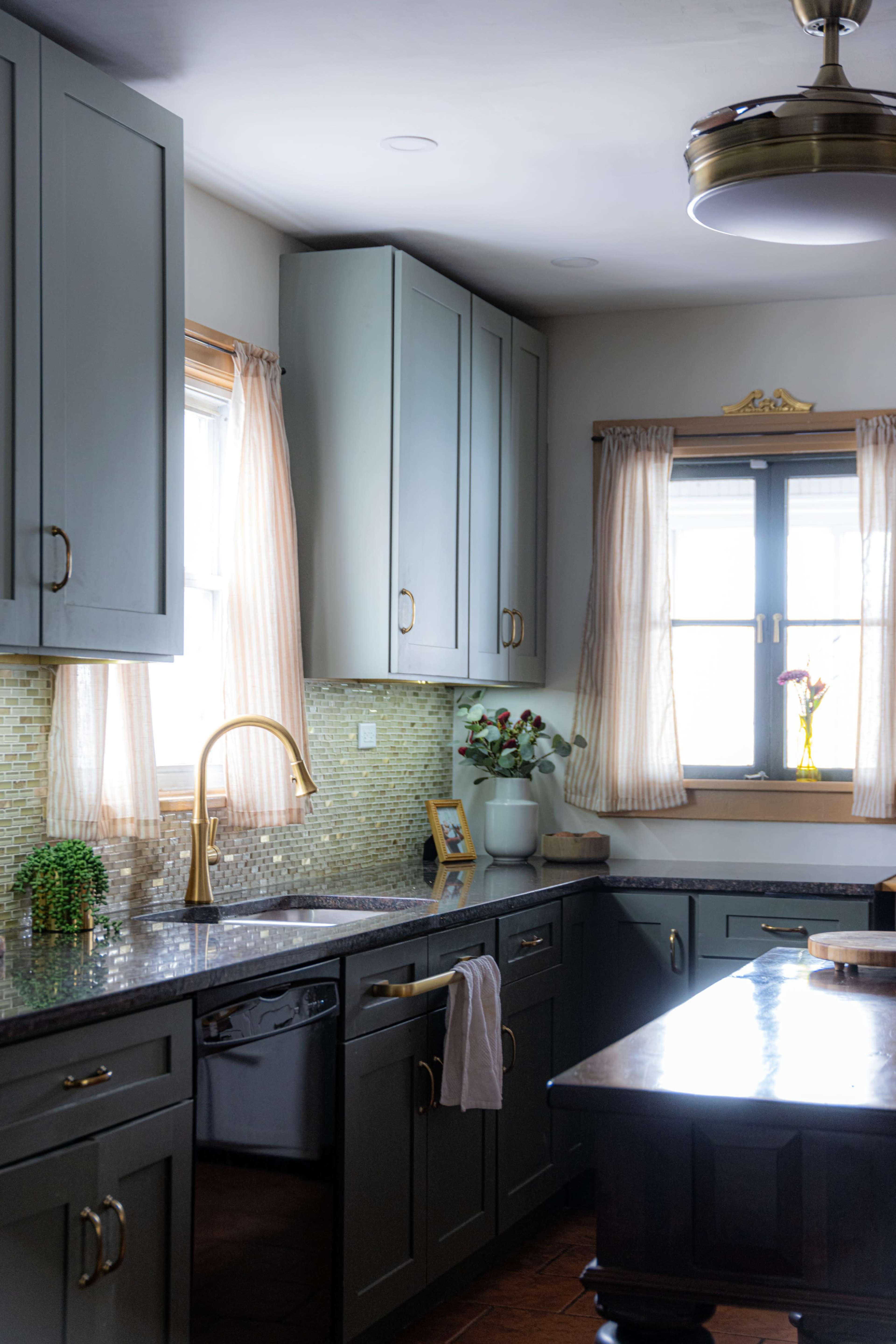 The kitchen features gray cabinetry, a granite countertop, a modern faucet, and natural light streaming through the windows.