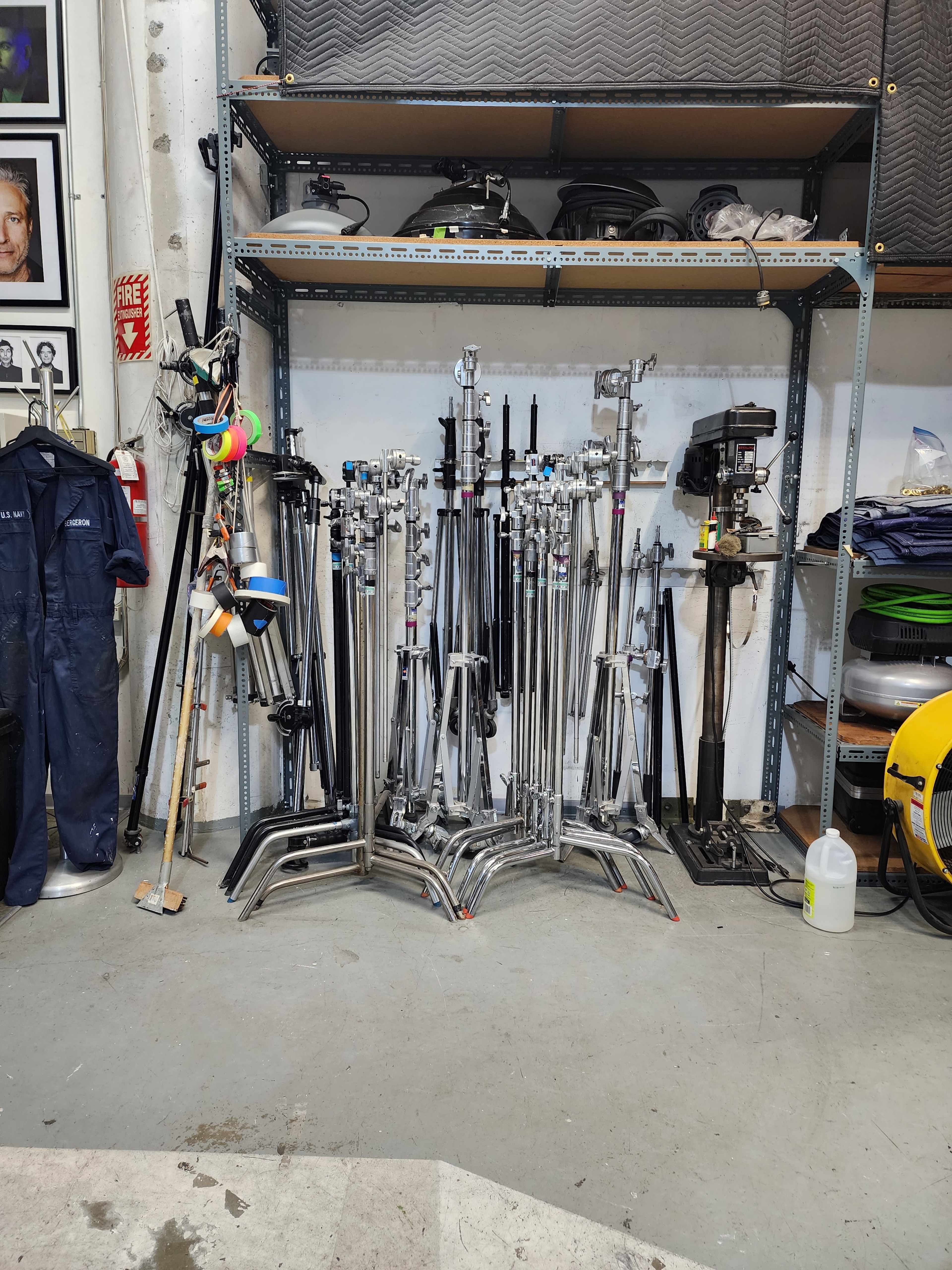A collection of various photography and lighting stands is neatly arranged on a shelf in a storage area.