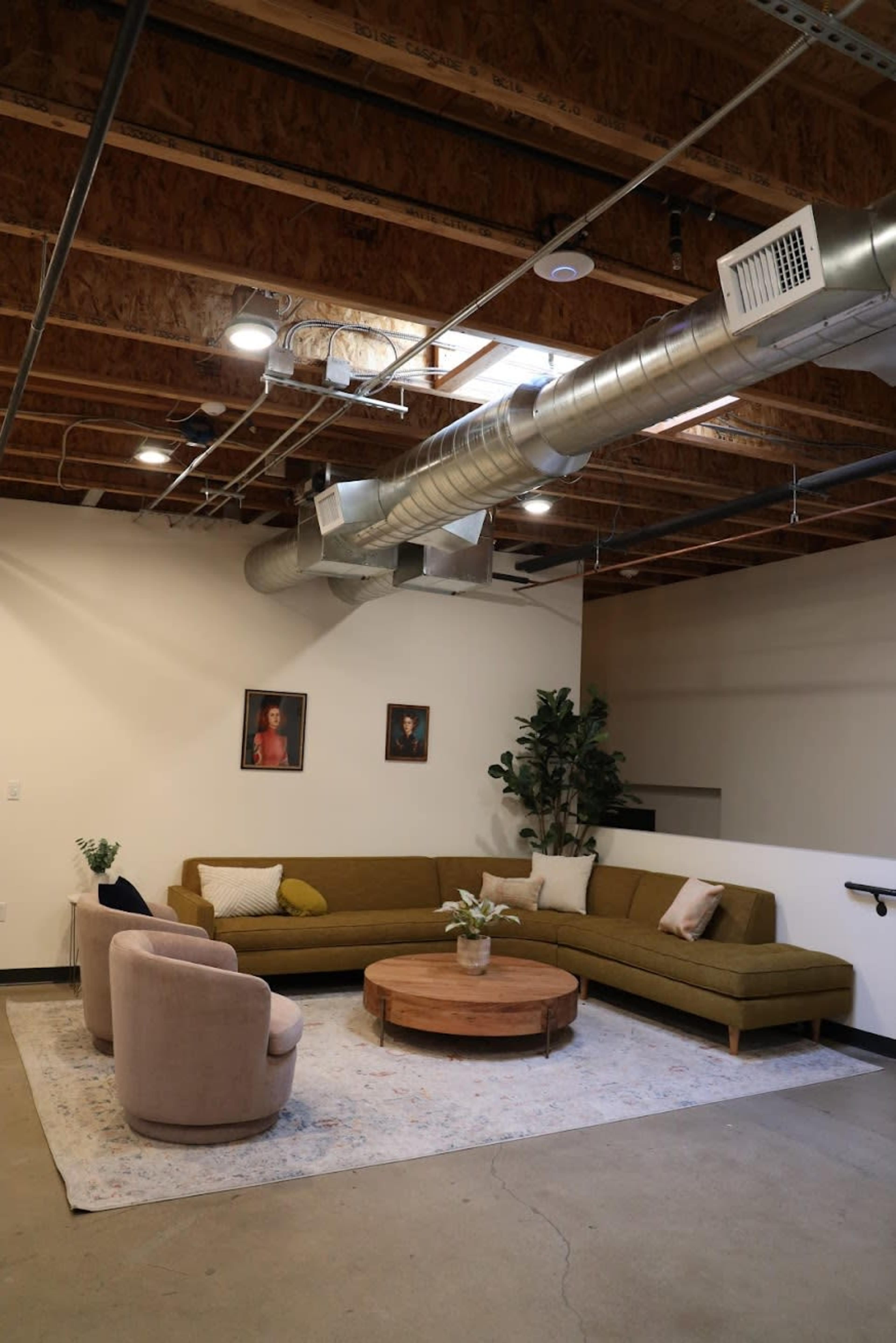 The image shows a modern living room with a large olive green sectional sofa, two light-colored armchairs, a round wooden coffee table, and a decorative rug under soft lighting from ceiling fixtures.