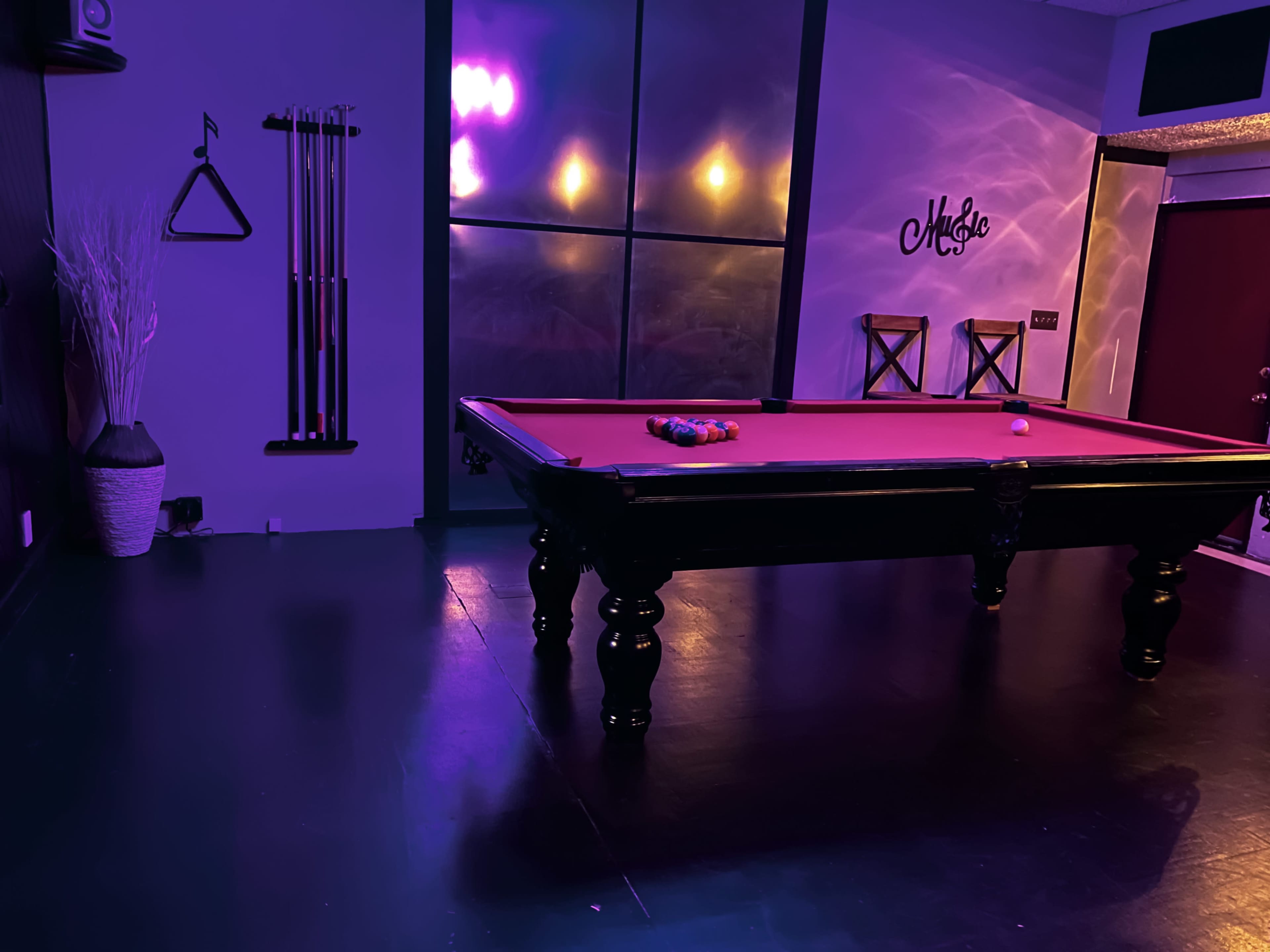 A dimly lit room featuring a purple pool table with a triangle of billiard balls resting on it and two barstools in the background.